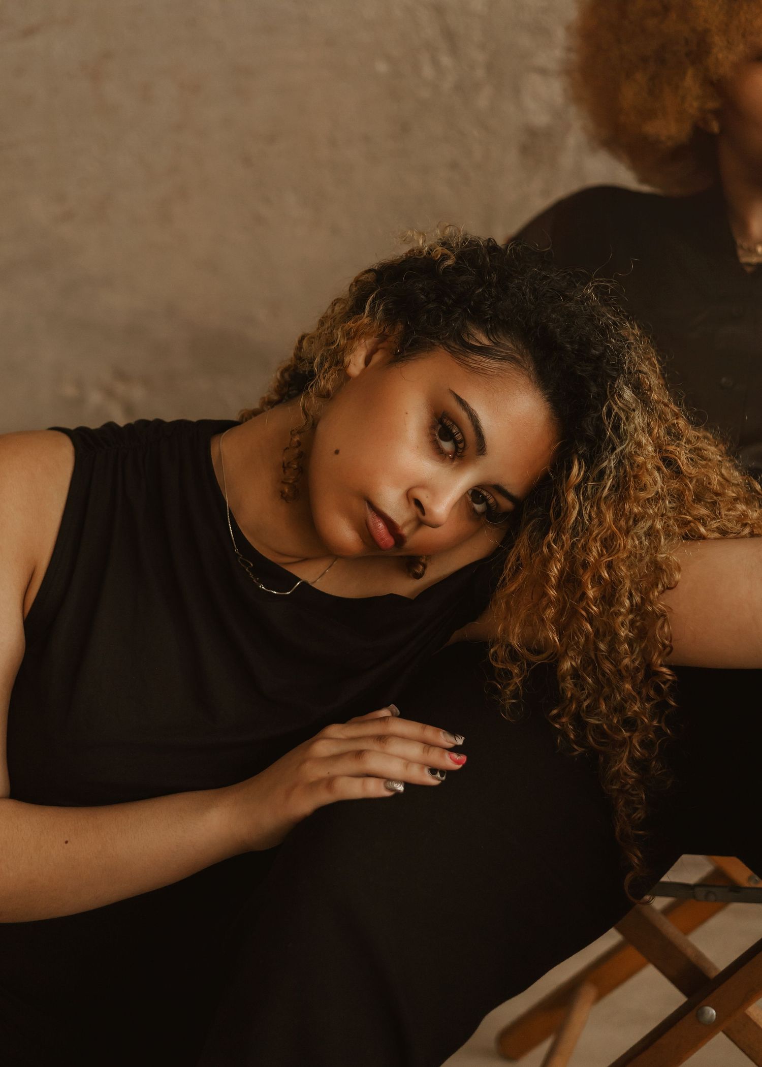 Person with curly brown hair wearing a black top lying on a light colored surface in a series of artistic poses.