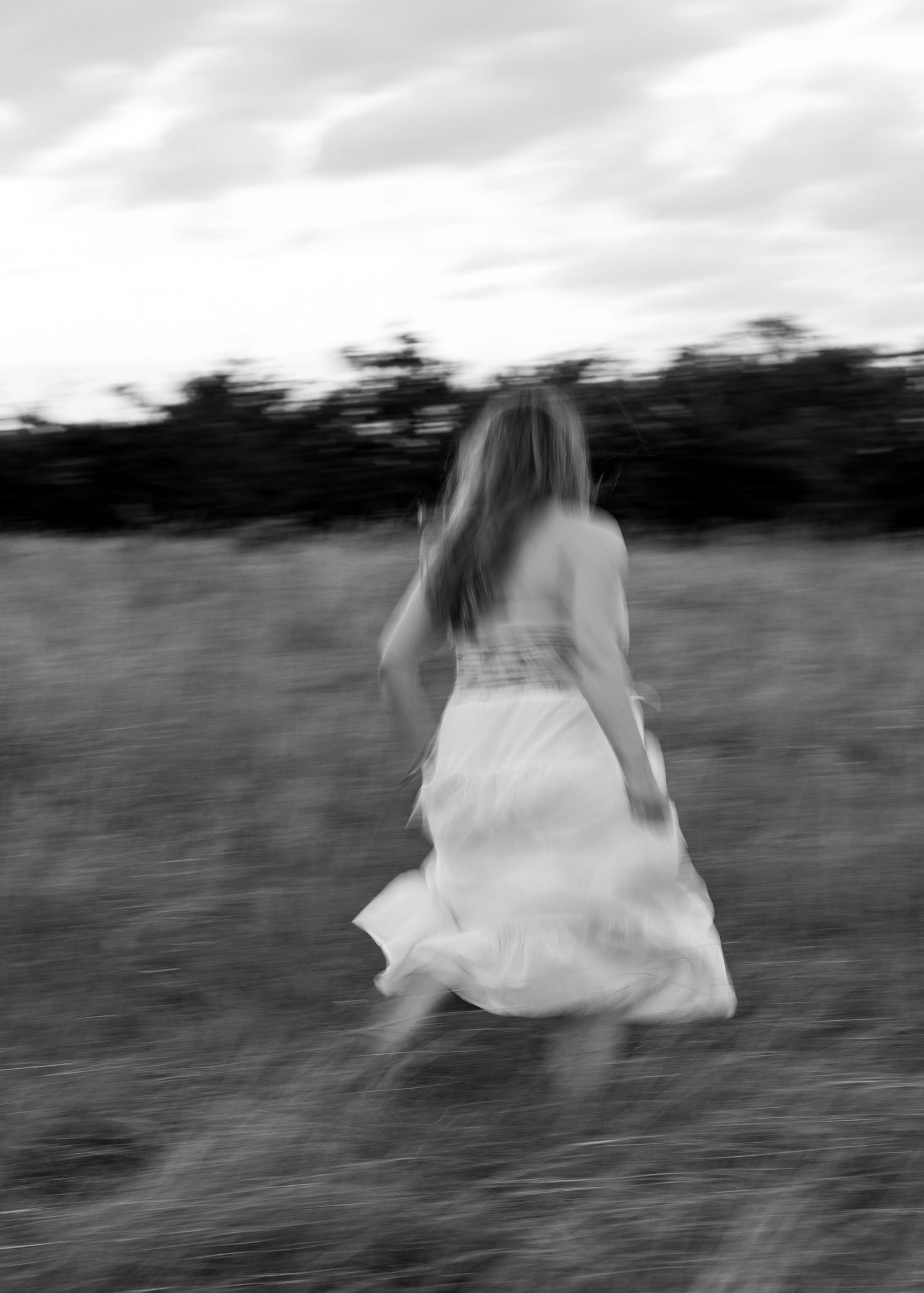 Black and white photo of a woman in a white dress running through a field with motion blur.