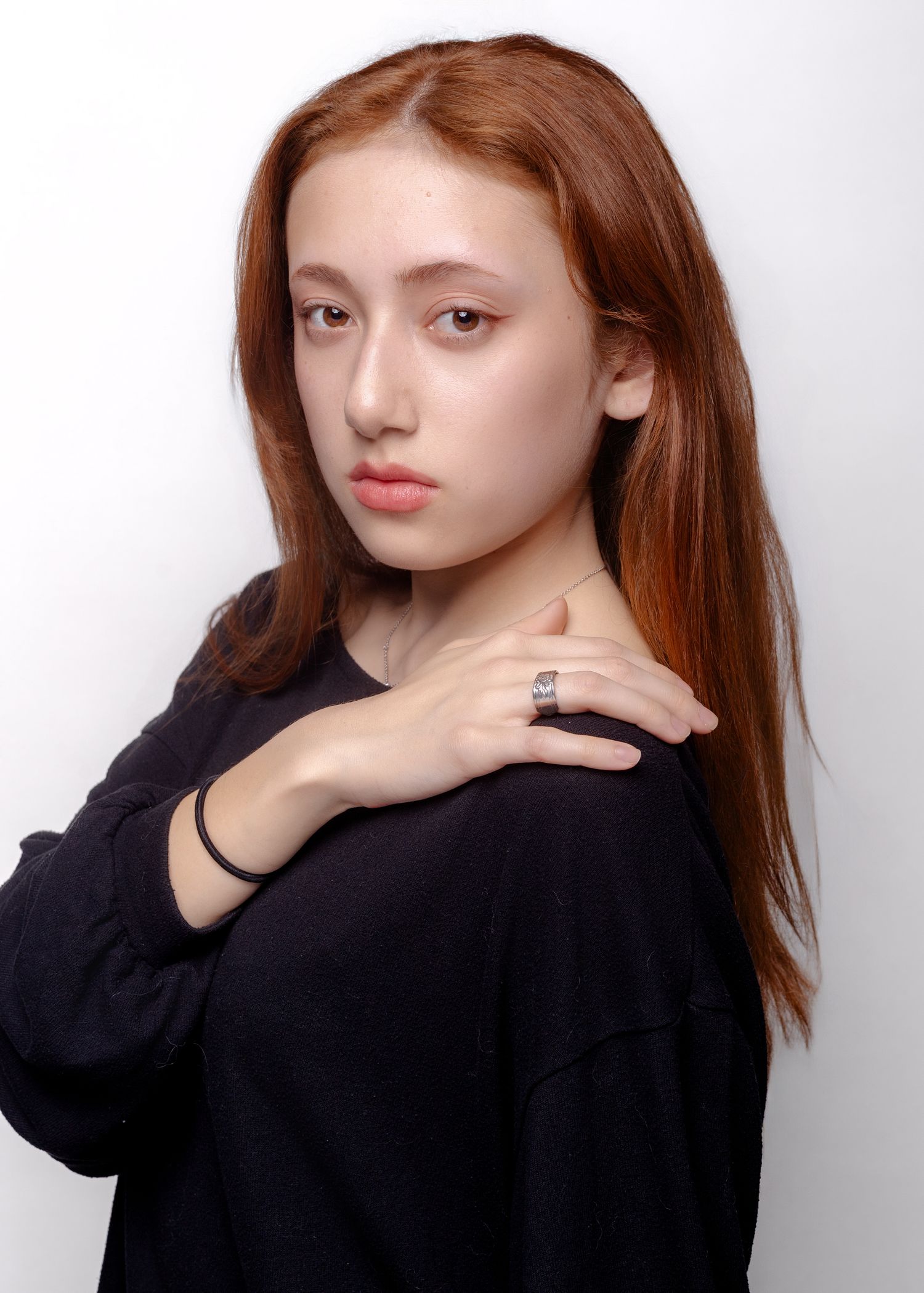 Person with long red hair poses expressively in black top against white background.