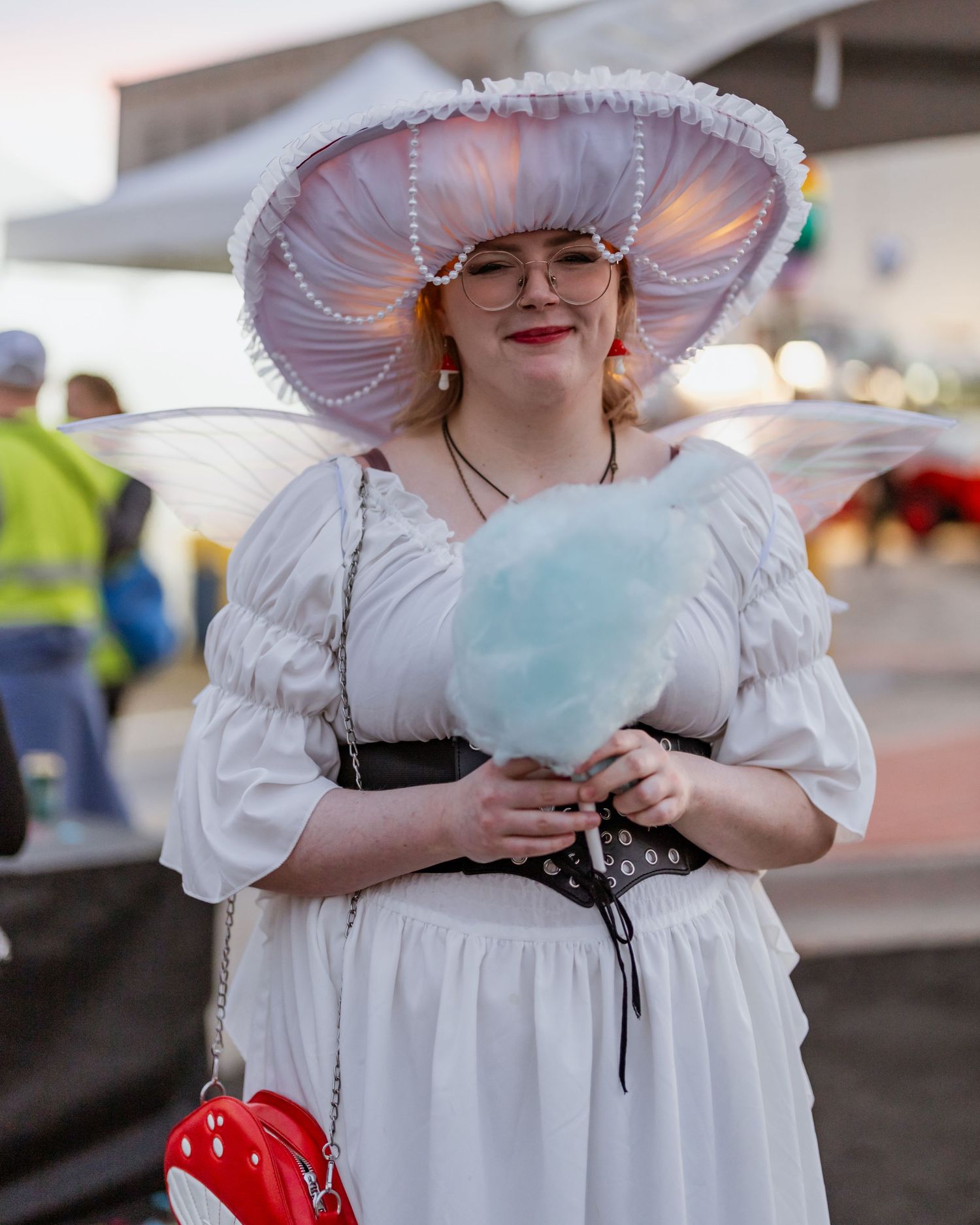 Person in white Victorian dress holding cotton candy at a carnival.