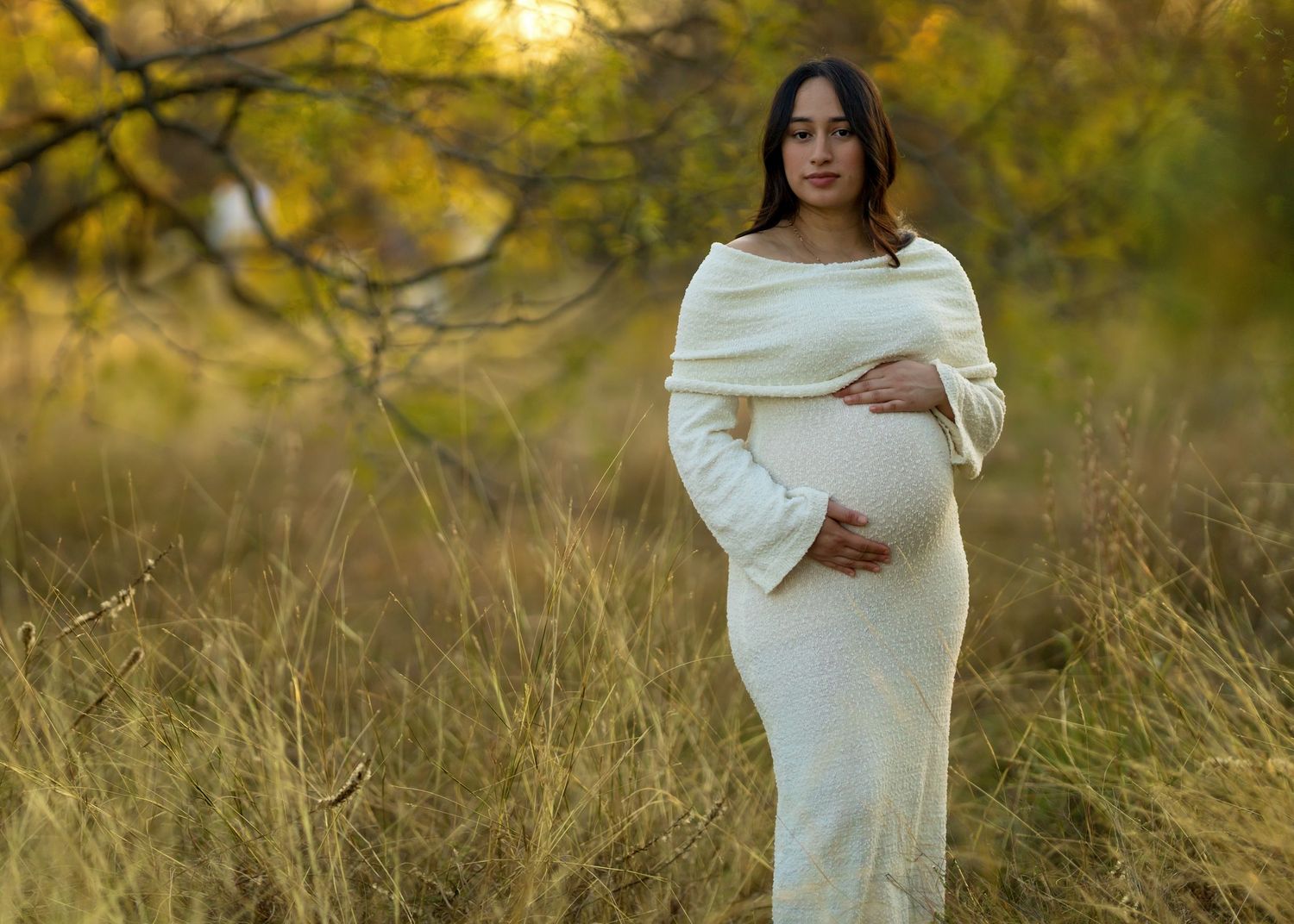 Silhouette of a person wrapped in white fabric against autumn foliage at sunset.