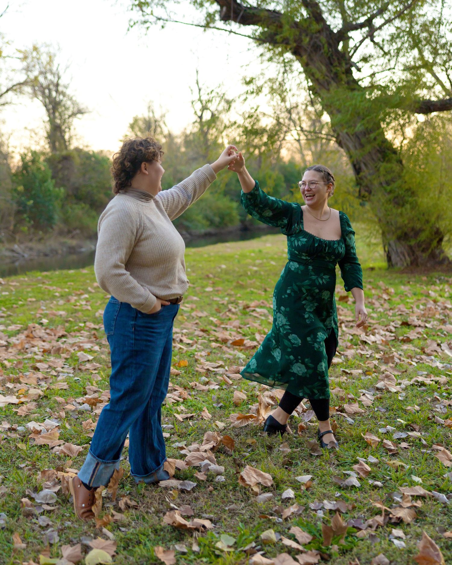 Playful couple dancing and twirling in a leaf-covered park during autumn.