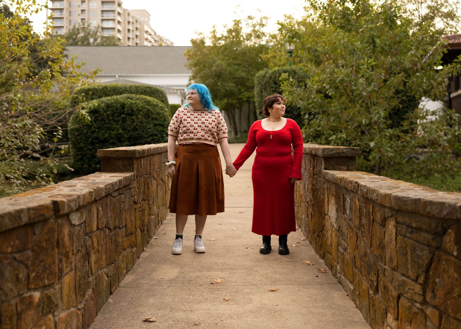 Stone bridge pathway with people walking in autumn park setting.