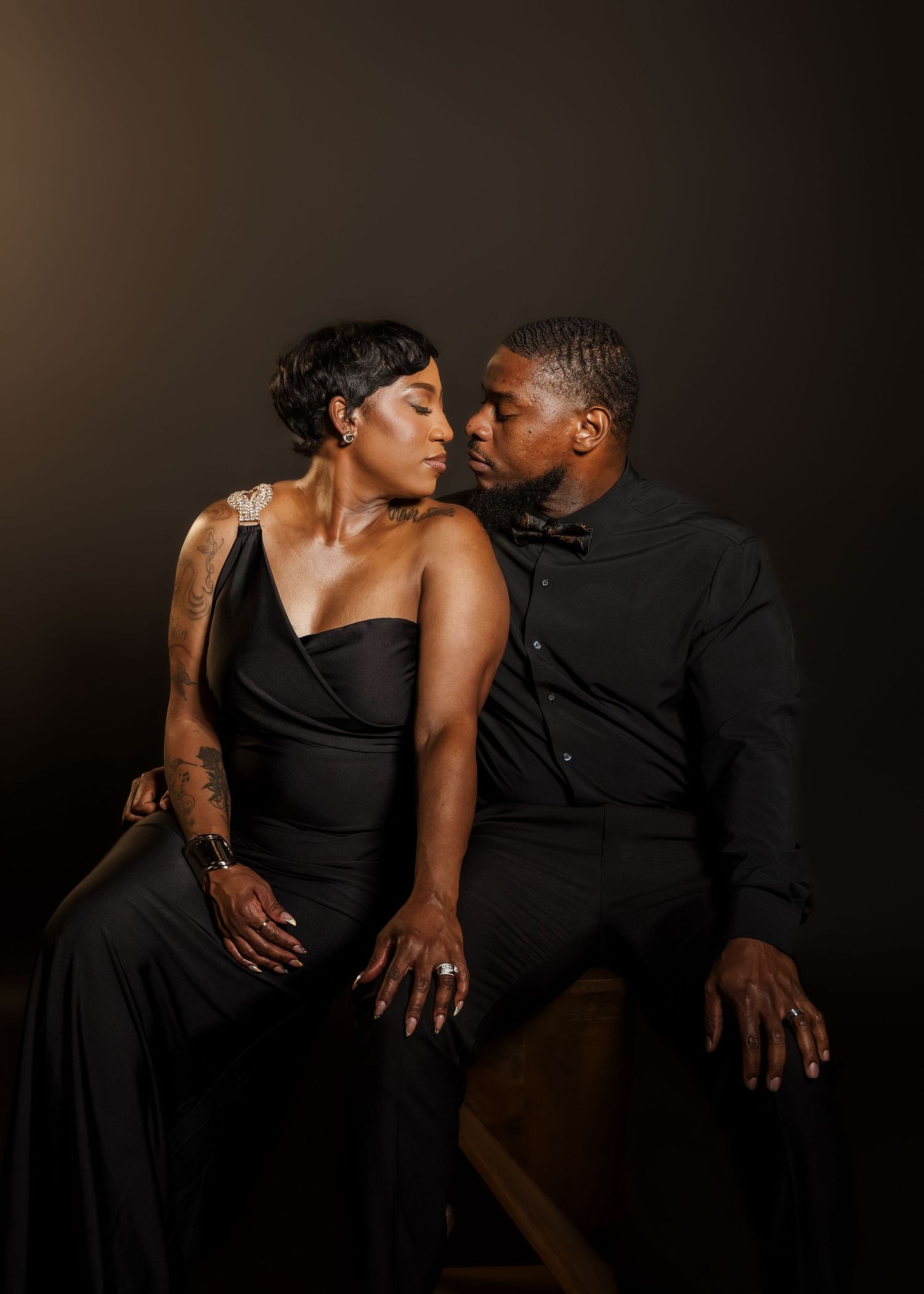 Elegant couple in matching black outfits sharing a romantic moment during a professional photo shoot.