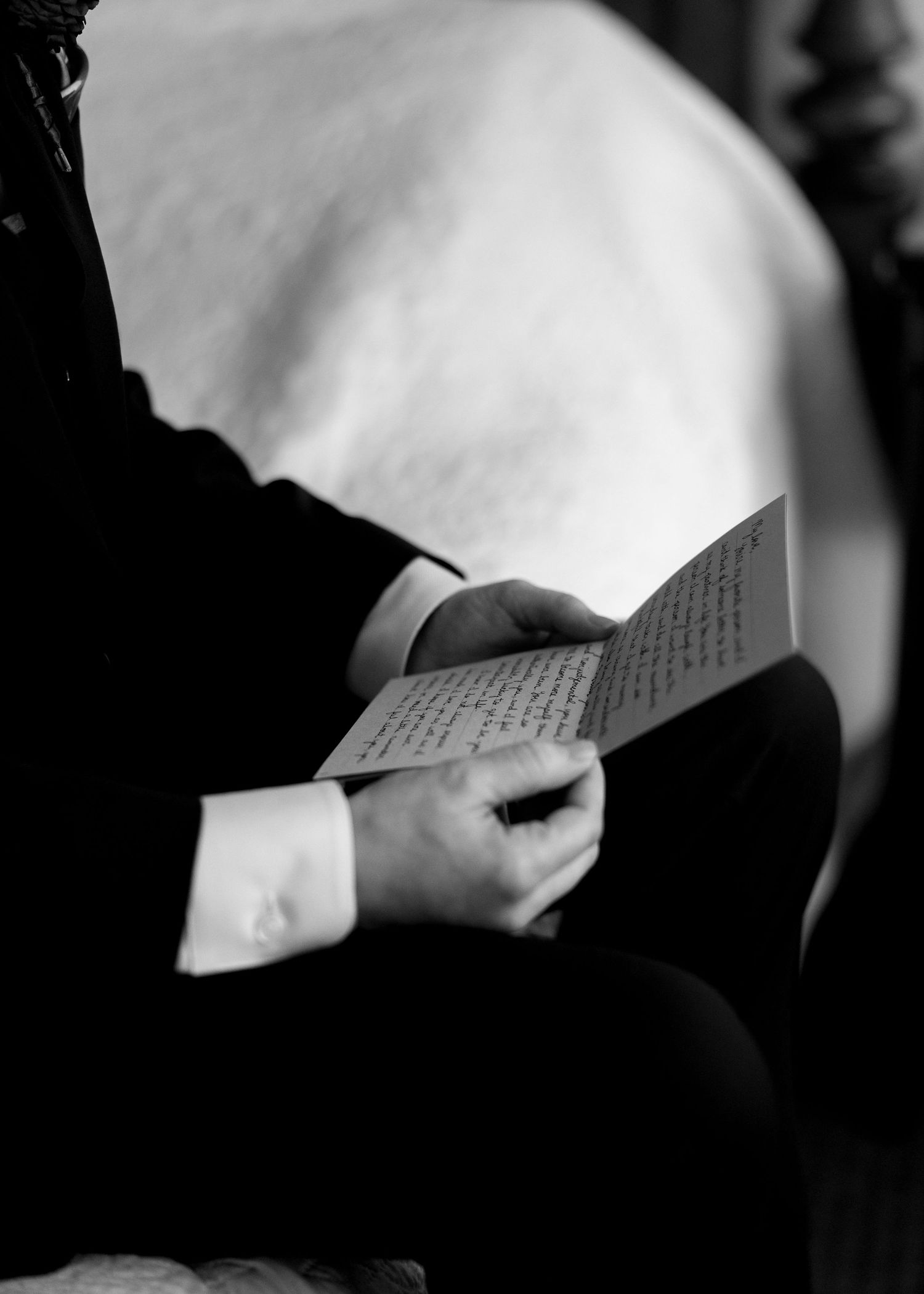Groom reading handwritten love letter from bride in black and white wedding day photo.