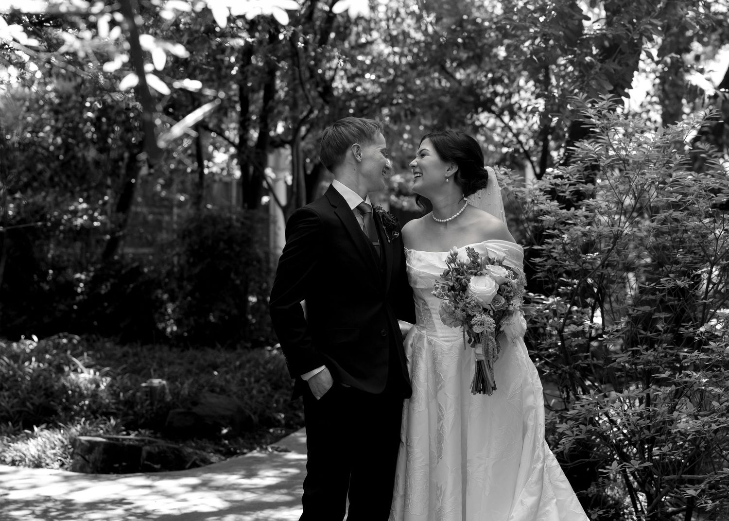 Black and white wedding photo of bride and groom sharing a romantic moment in a lush garden setting.