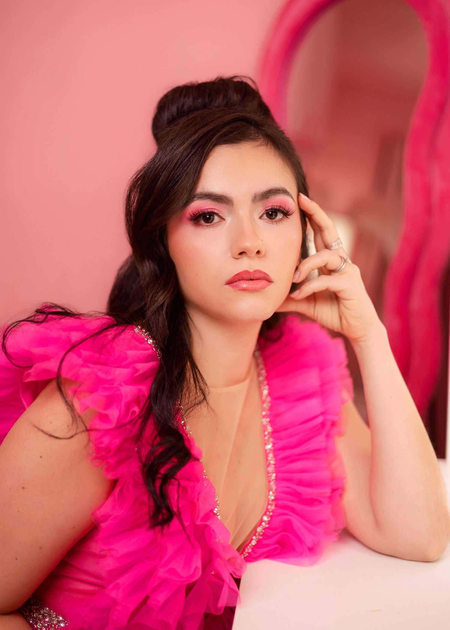 Model in vibrant hot pink tulle dress poses against pink backdrop in glamorous fashion photoshoot.