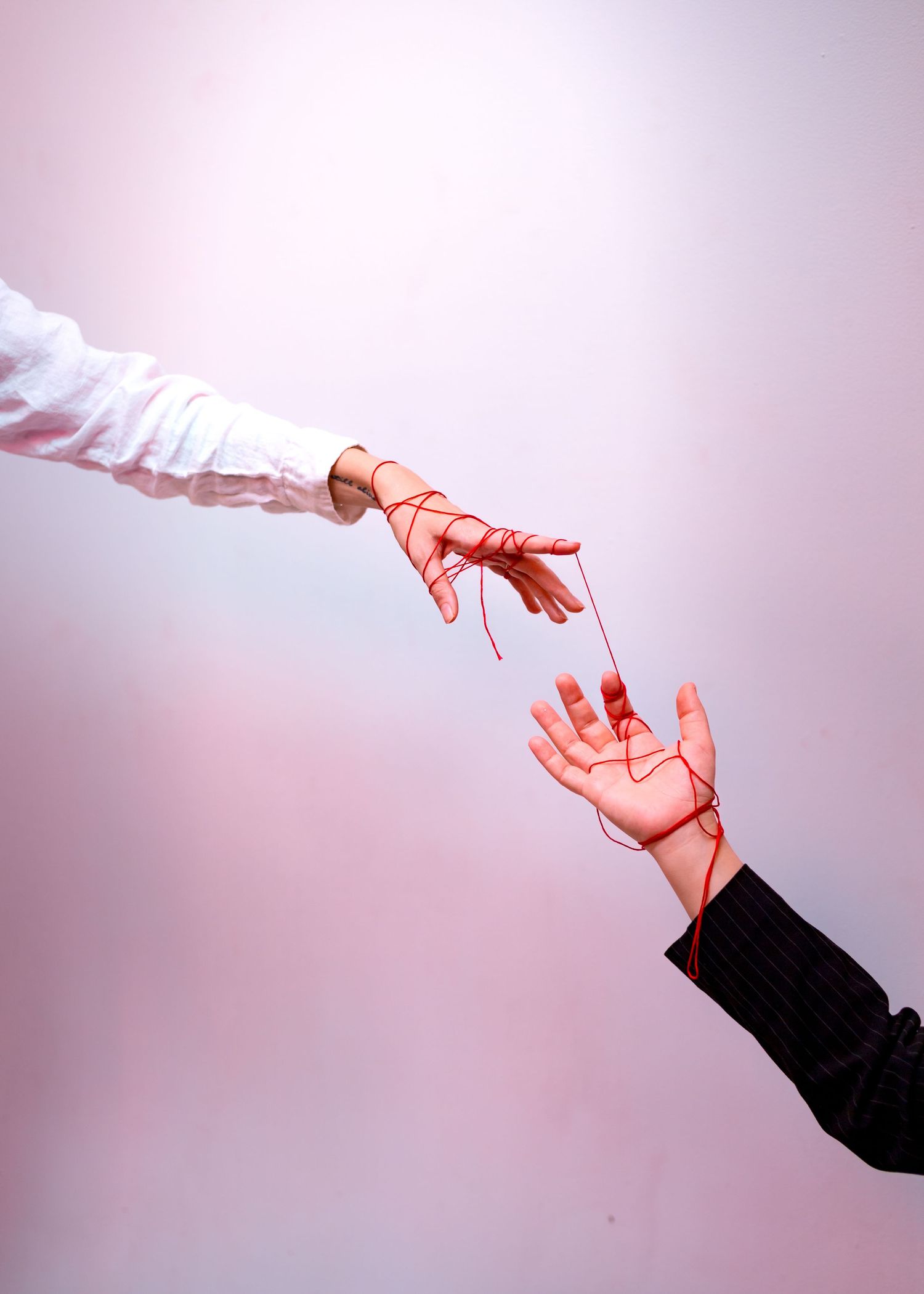 Artistic close-up of two hands reaching toward each other against pink background.