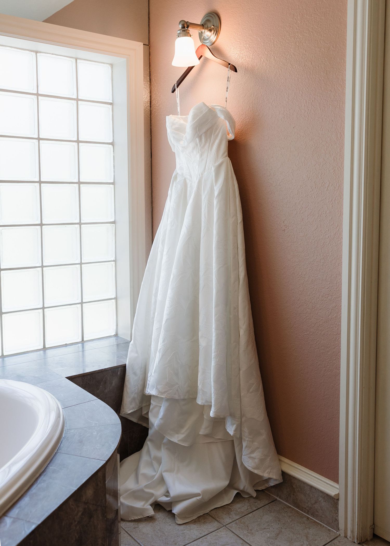 White strapless wedding gown hanging on a wall sconce light in an elegant bathroom before the ceremony.