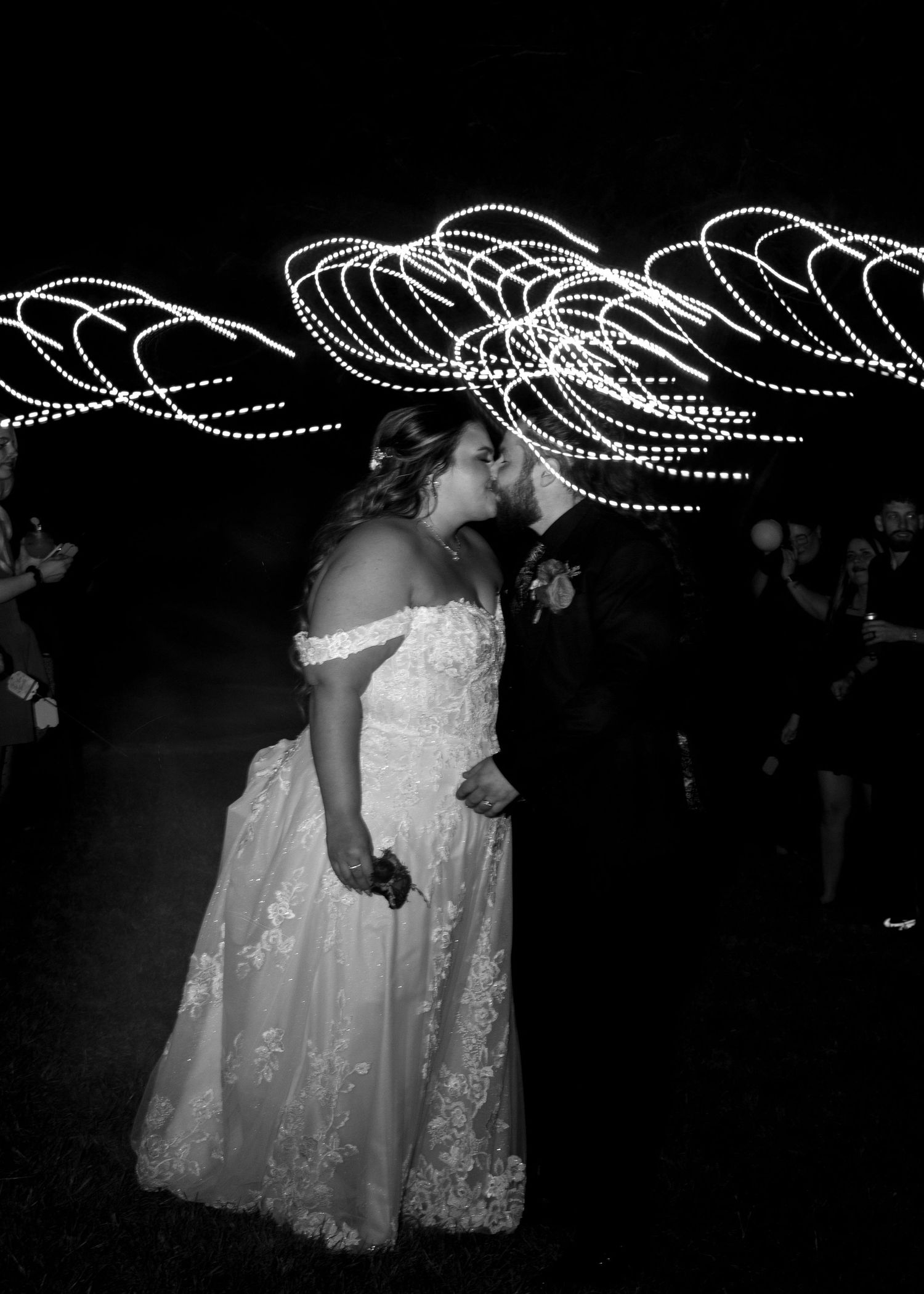 Black and white photo of newlyweds kissing with stunning light painting swirls at night wedding reception.