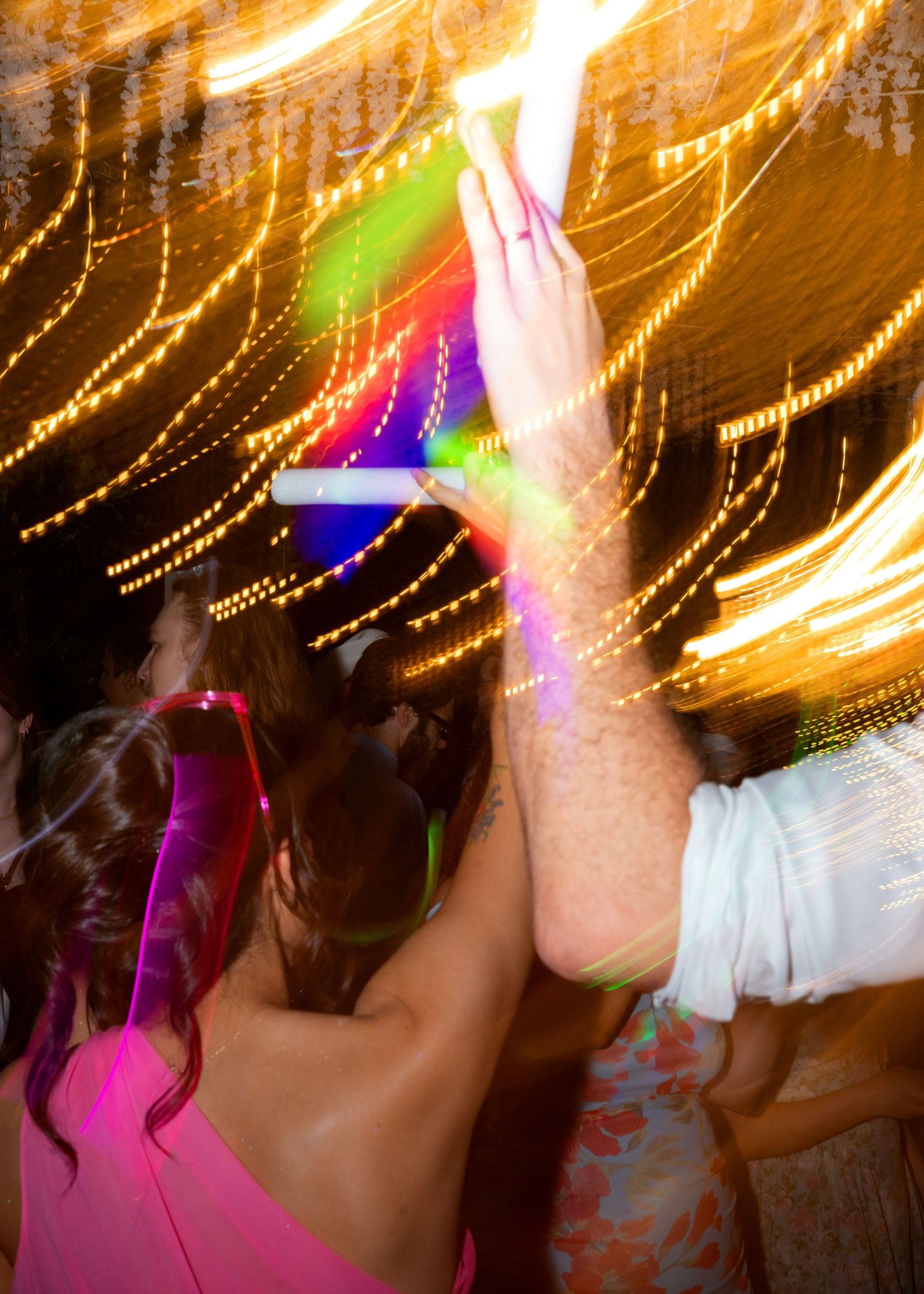 People dancing at a vibrant party with colorful light streaks and glowing decorations in the background.