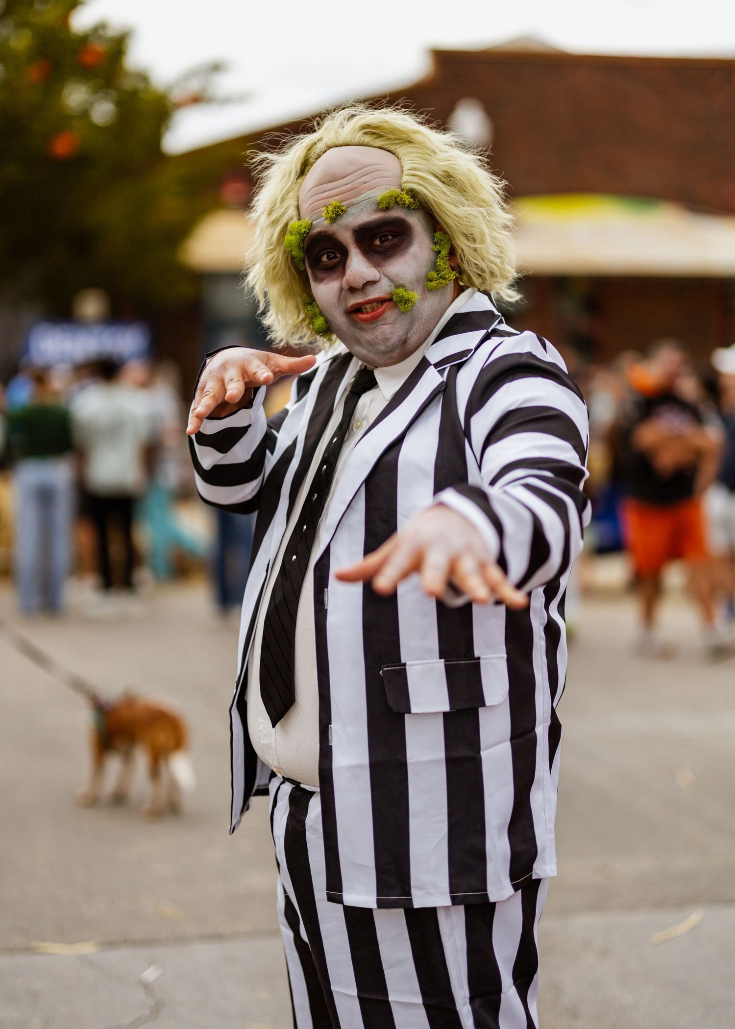 A person in a black and white striped Beetlejuice costume poses and dances at an outdoor event.