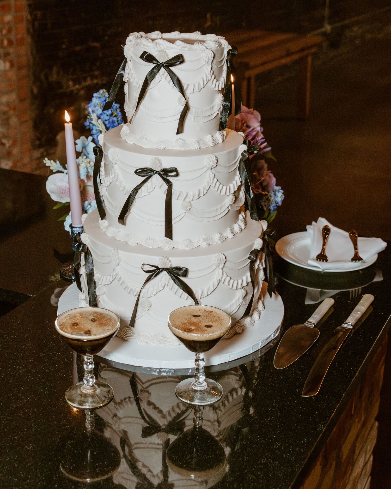 Elegant white wedding cake with black ribbon details displayed next to champagne glasses.