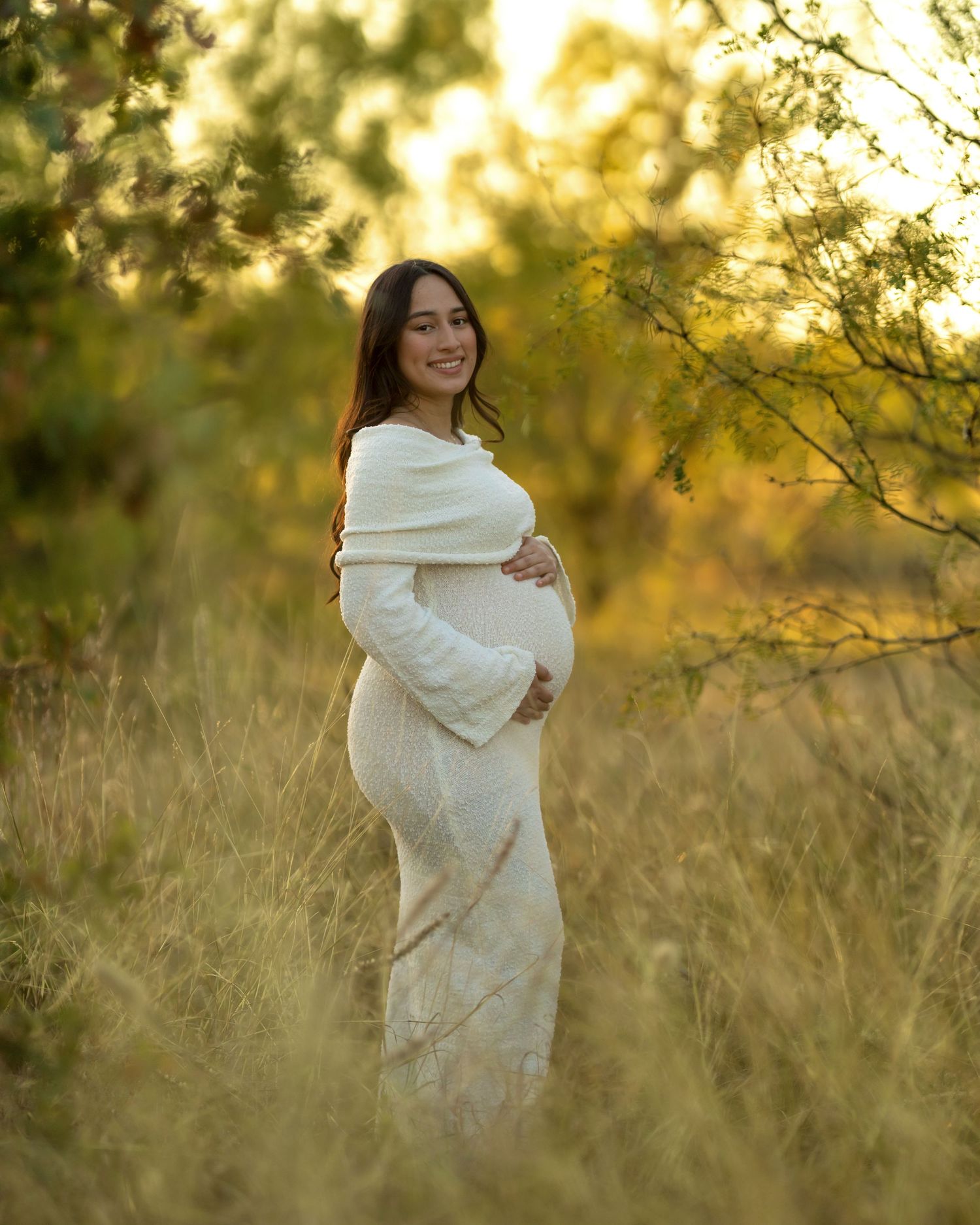 A figure in a white dress stands in tall grass during golden hour sunset.