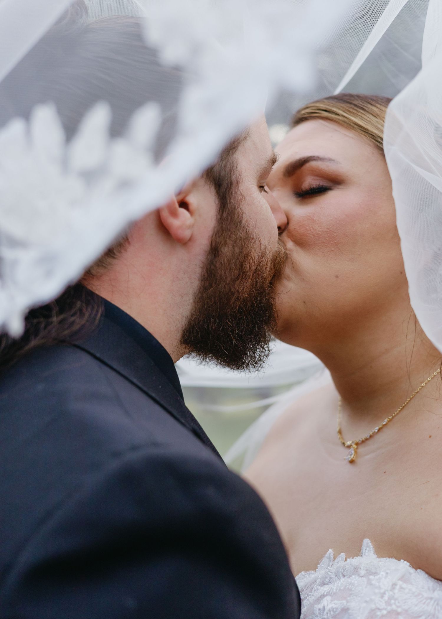 Bride and groom sharing a romantic kiss under a floral wedding veil on their special day.