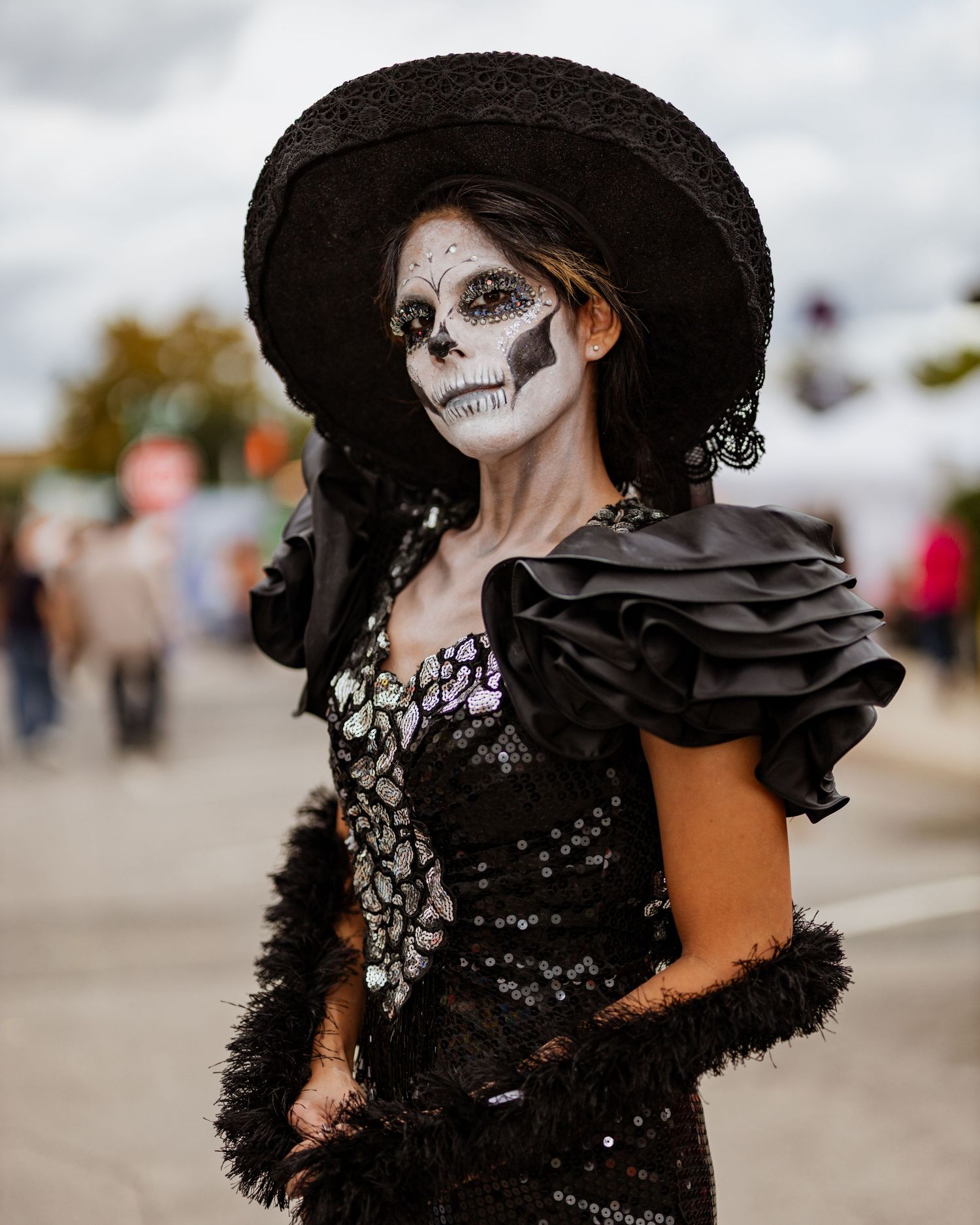 A dramatic gothic costume featuring a black lace dress, wide-brimmed hat, and skeleton face paint.