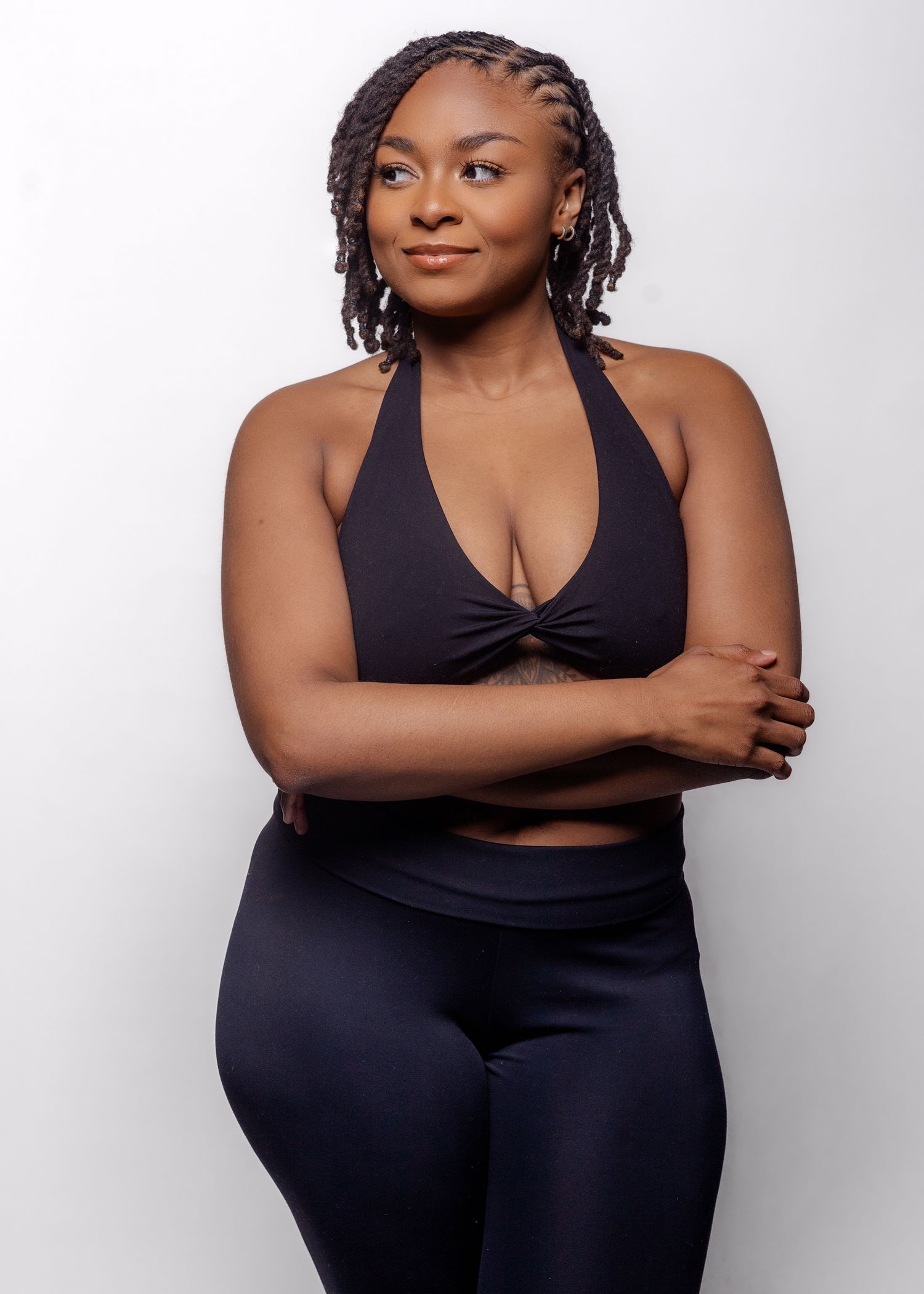 Athletic figure in black workout attire poses confidently against white background.