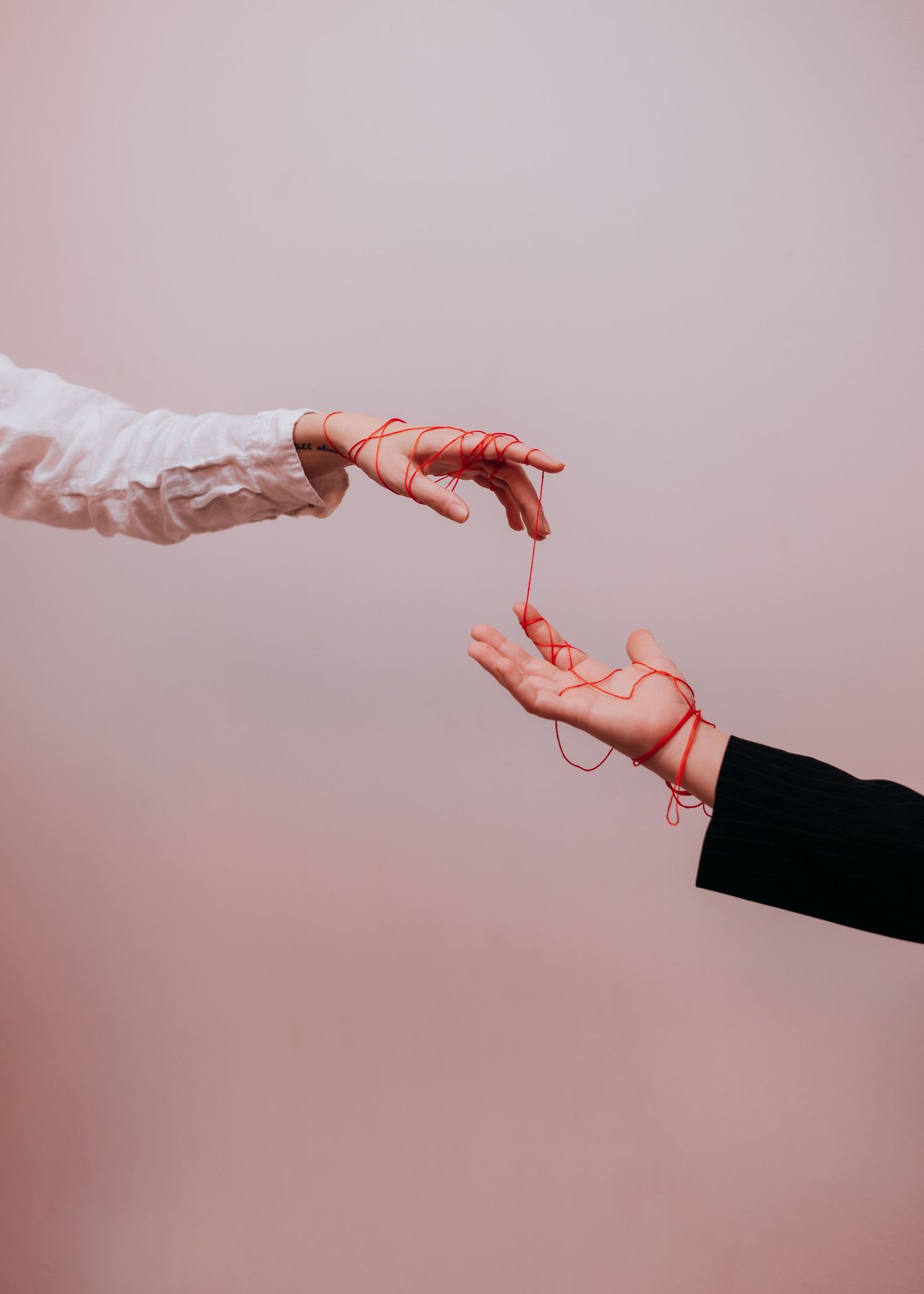 Two hands reaching towards each other against a pink background, one wearing white sleeve and one in black sleeve.