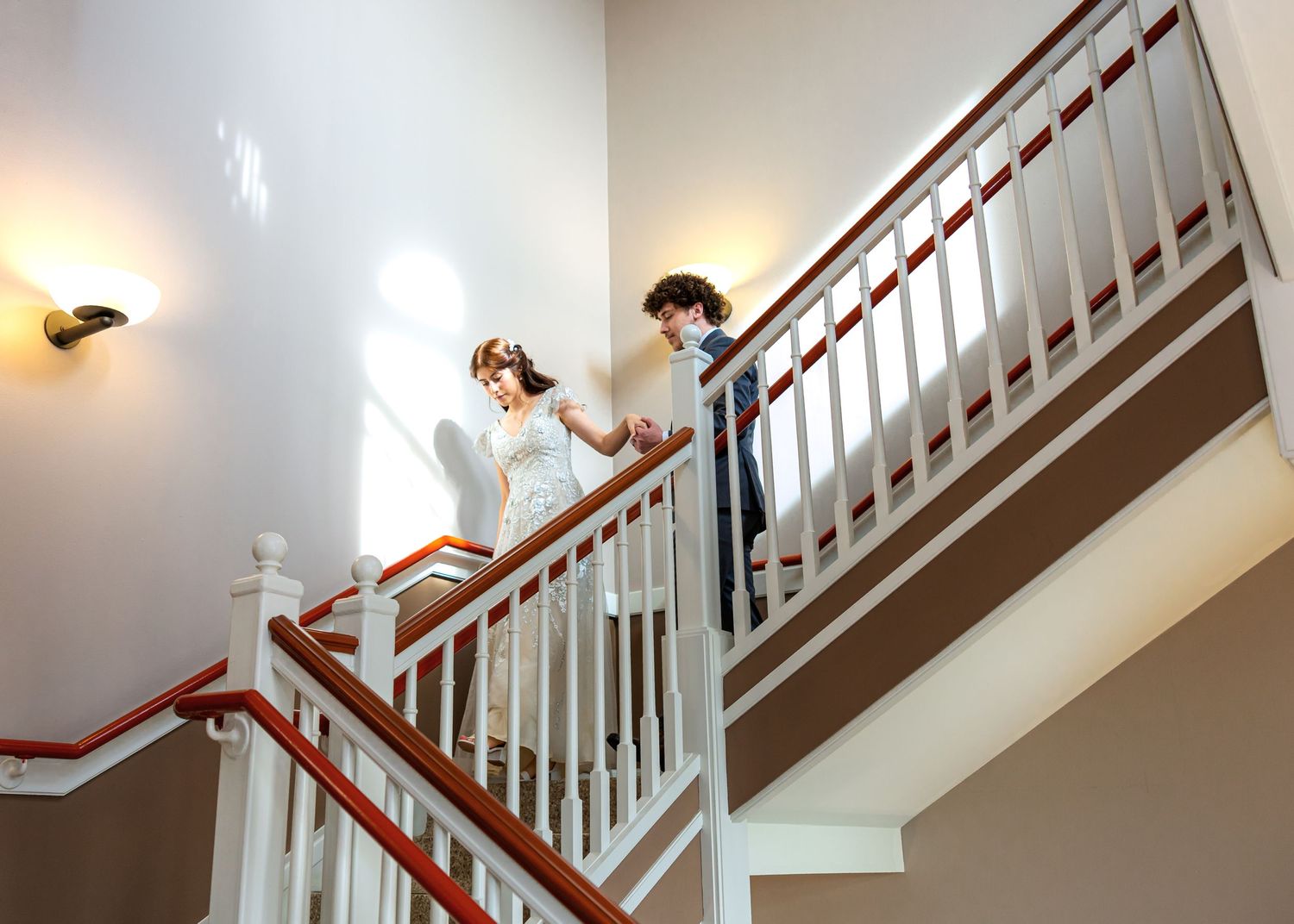 Interior staircase with white walls and wooden railings lit by natural light.
