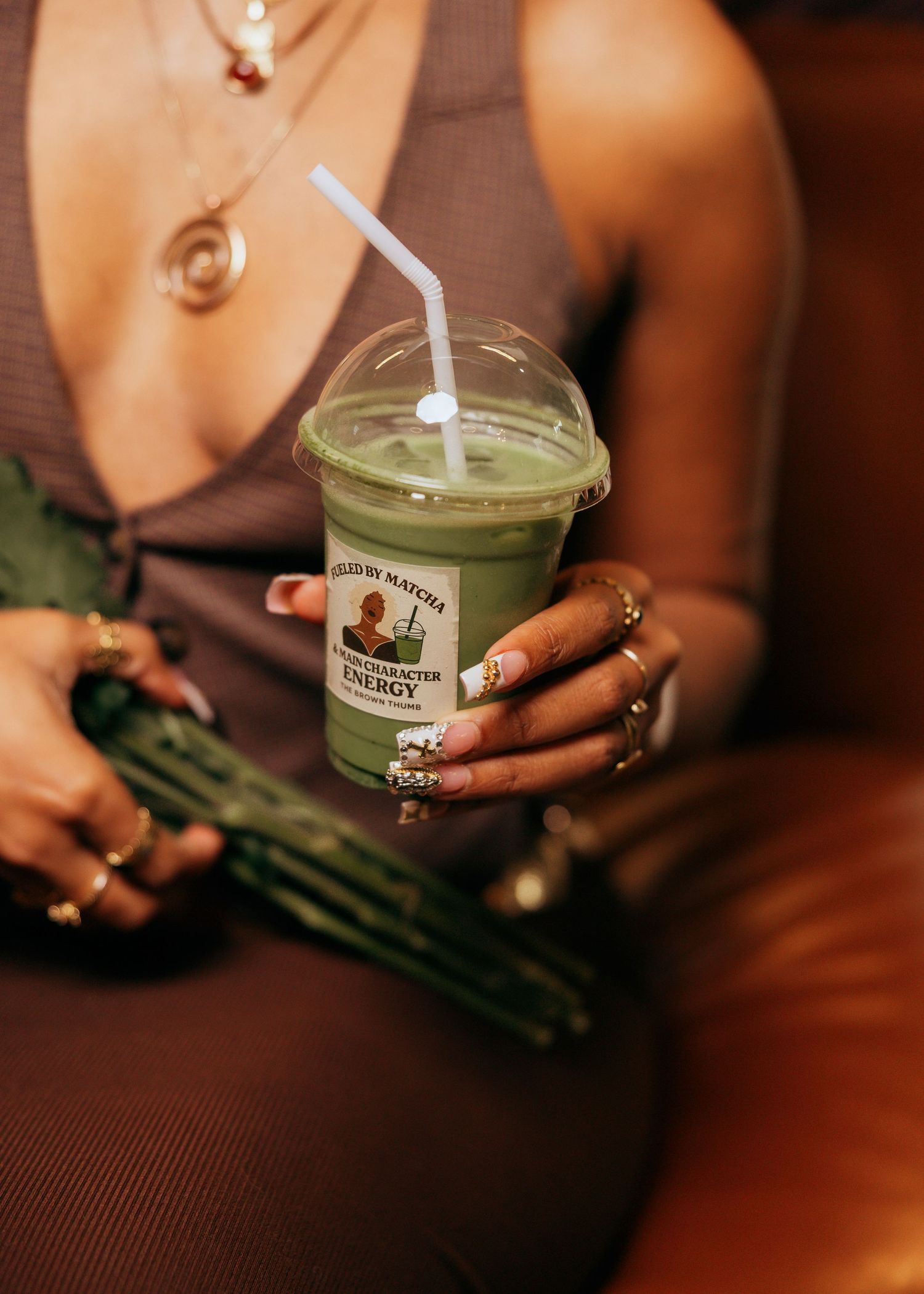 Hands holding a green smoothie drink with flowers in an atmospheric setting.