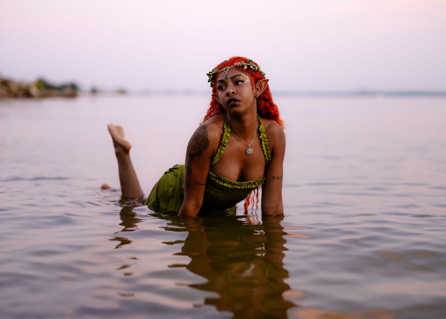 Ethereal water photoshoot featuring bright green dress and floral headpiece against sunset sky.