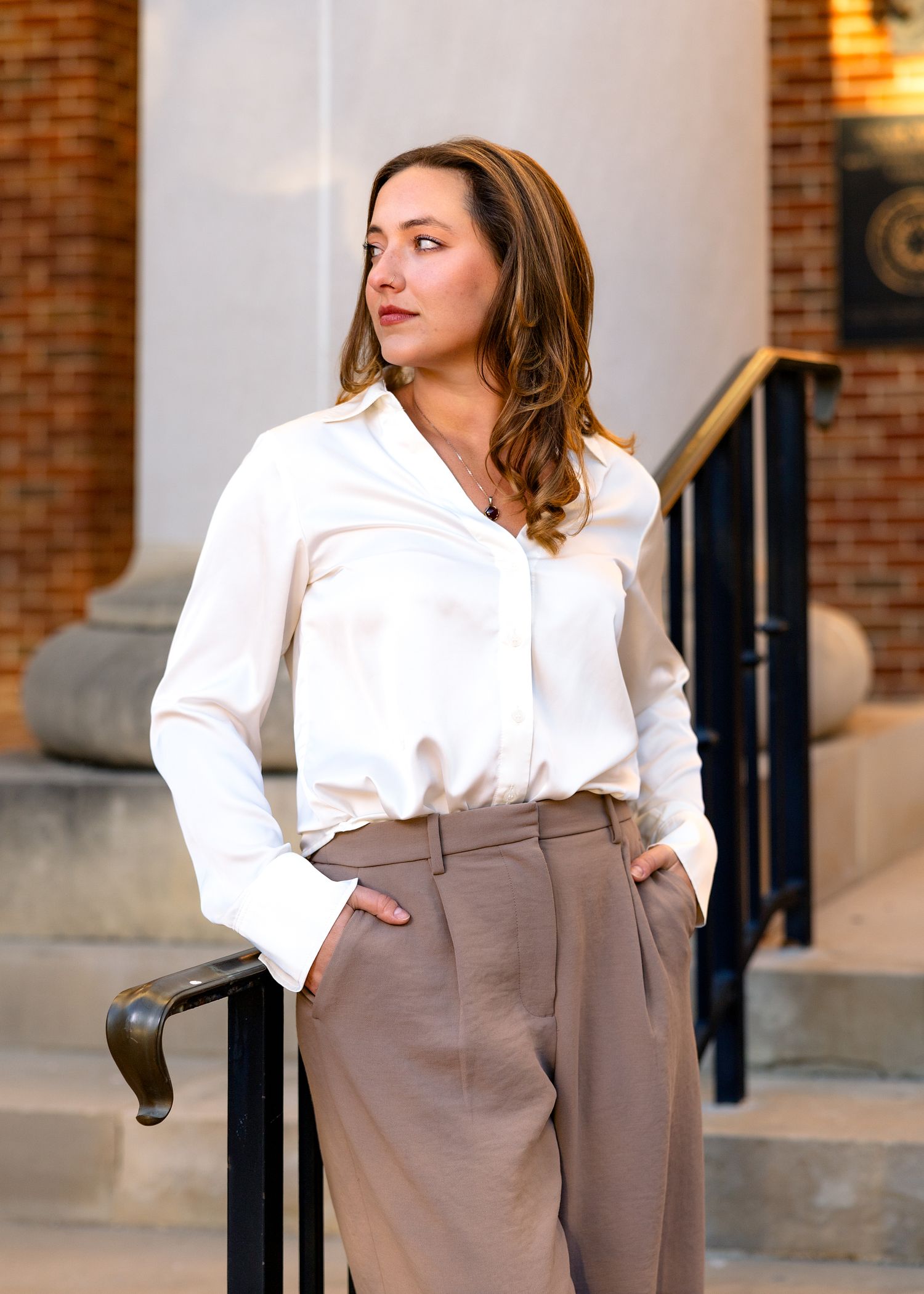 Fashion portrait in white blouse and wide-leg pants posed on outdoor steps.
