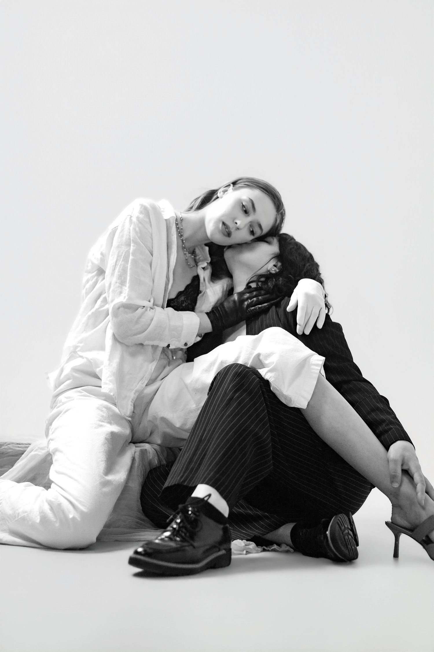 Black and white fashion photo featuring two models in contrasting outfits sitting on floor.