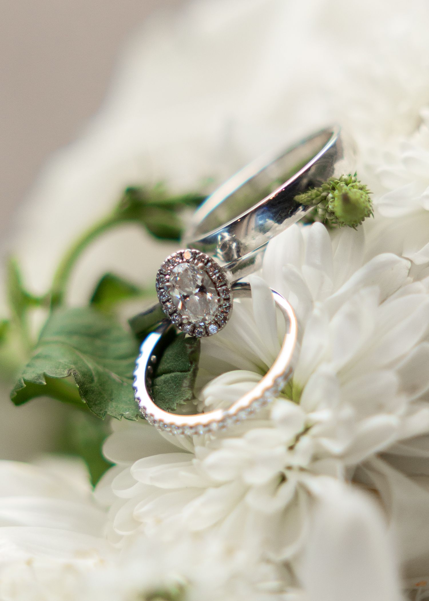 Diamond halo engagement ring and wedding bands resting on white flowers in bridal bouquet.