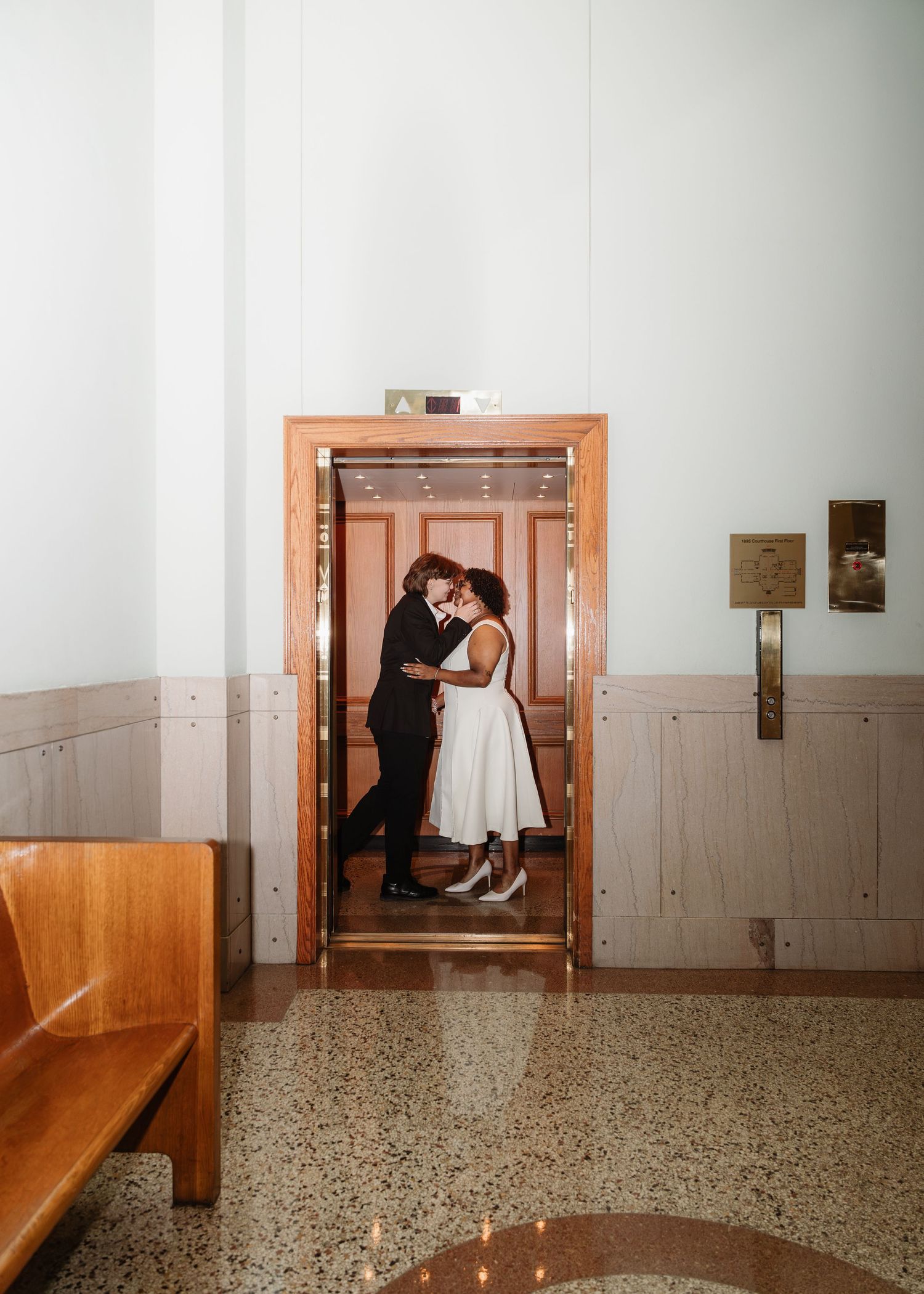 Newlywed couple sharing a kiss inside a vintage elevator during their wedding day photo session.