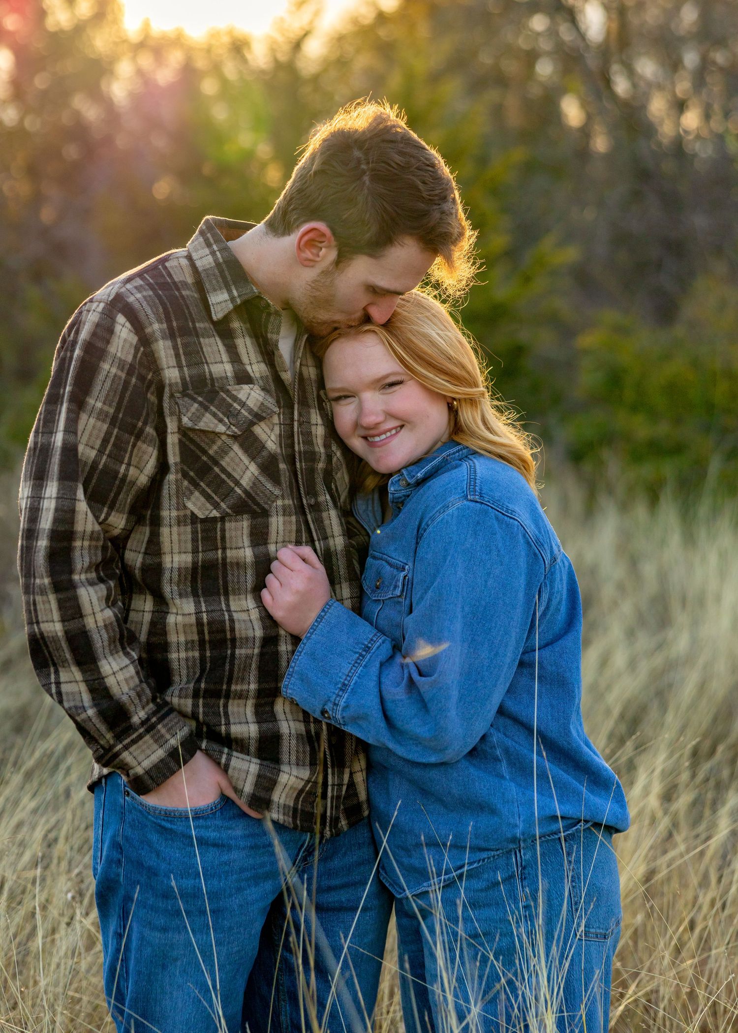 Couple laughing together in a field during golden hour, wearing casual denim and plaid.