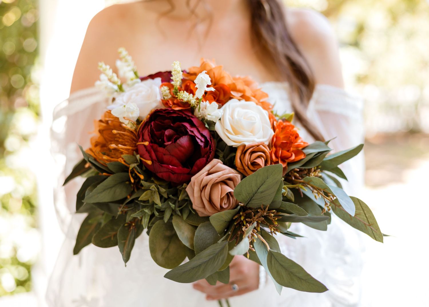 Bride holding a lush wedding bouquet with burgundy, rust, blush, and white blooms accented by eucalyptus greenery.
