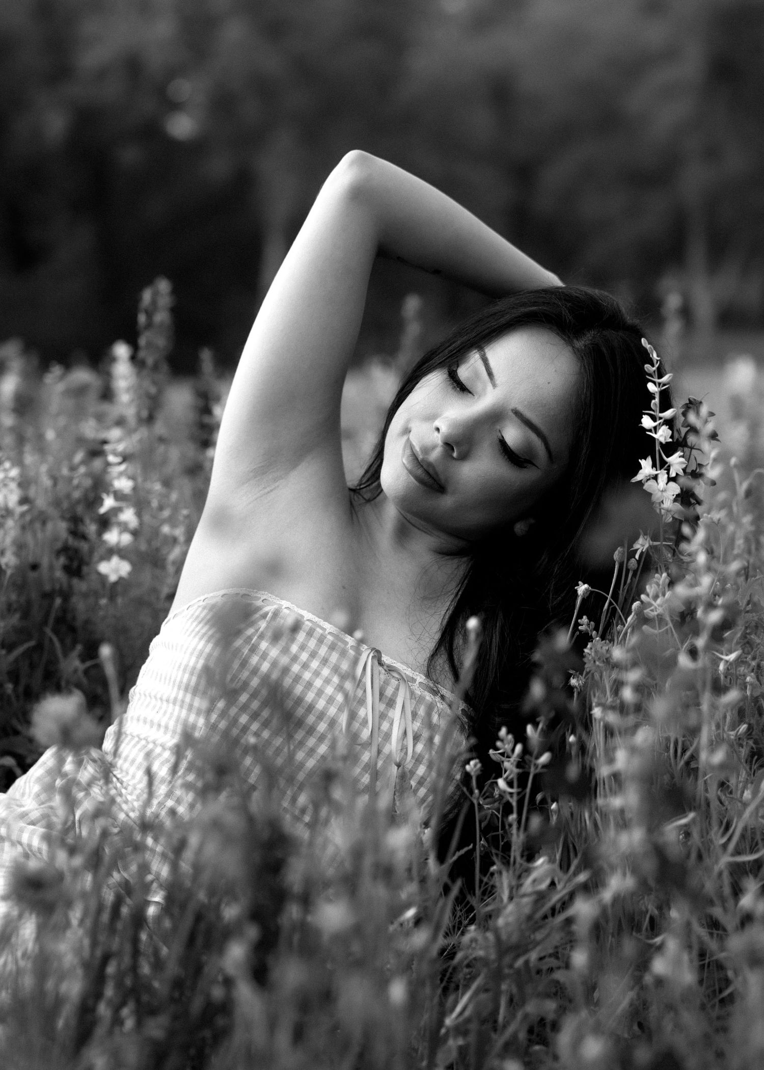 Black and white photo of a woman in a floral field, eyes closed, arm raised gracefully above her head.