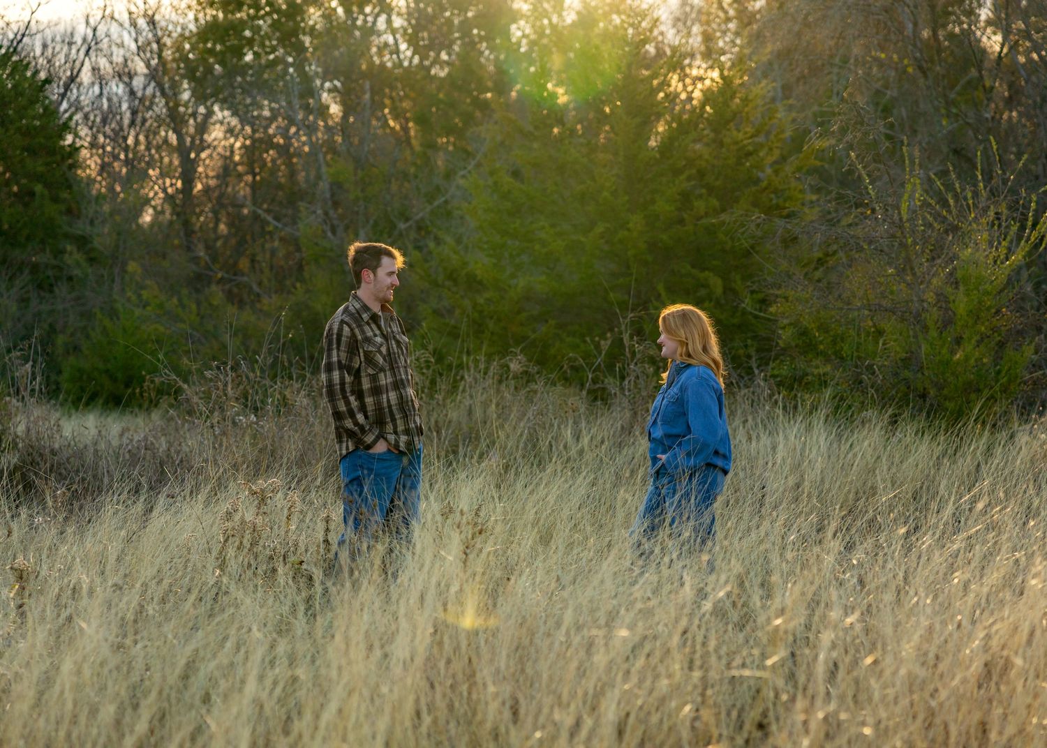 Silhouettes of two people walking through a sunlit field of tall grass.