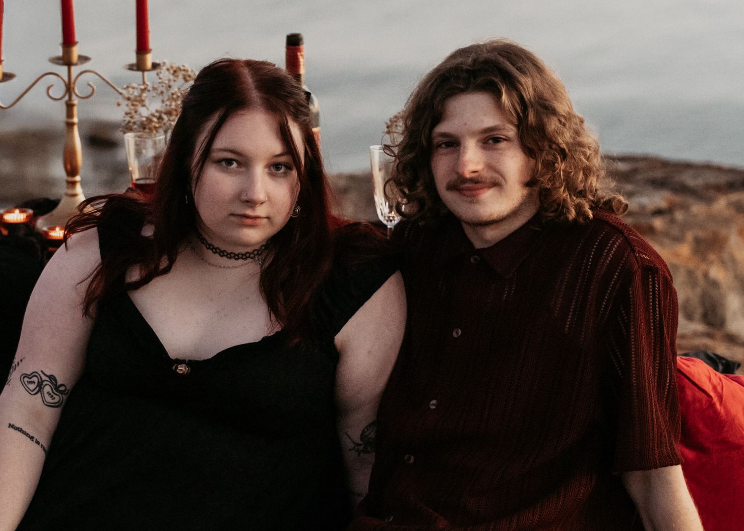Two people in dark clothing sitting together on a rocky cliff edge.