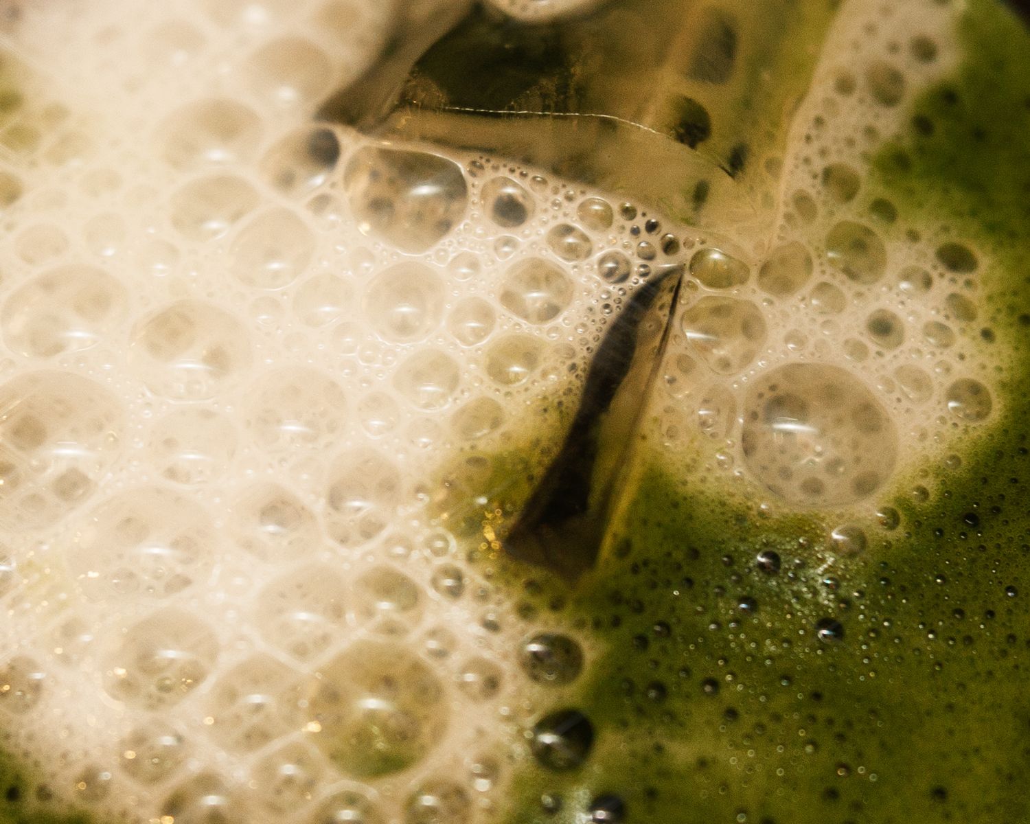 Frothy green matcha tea bubbles in a glass macro shot.