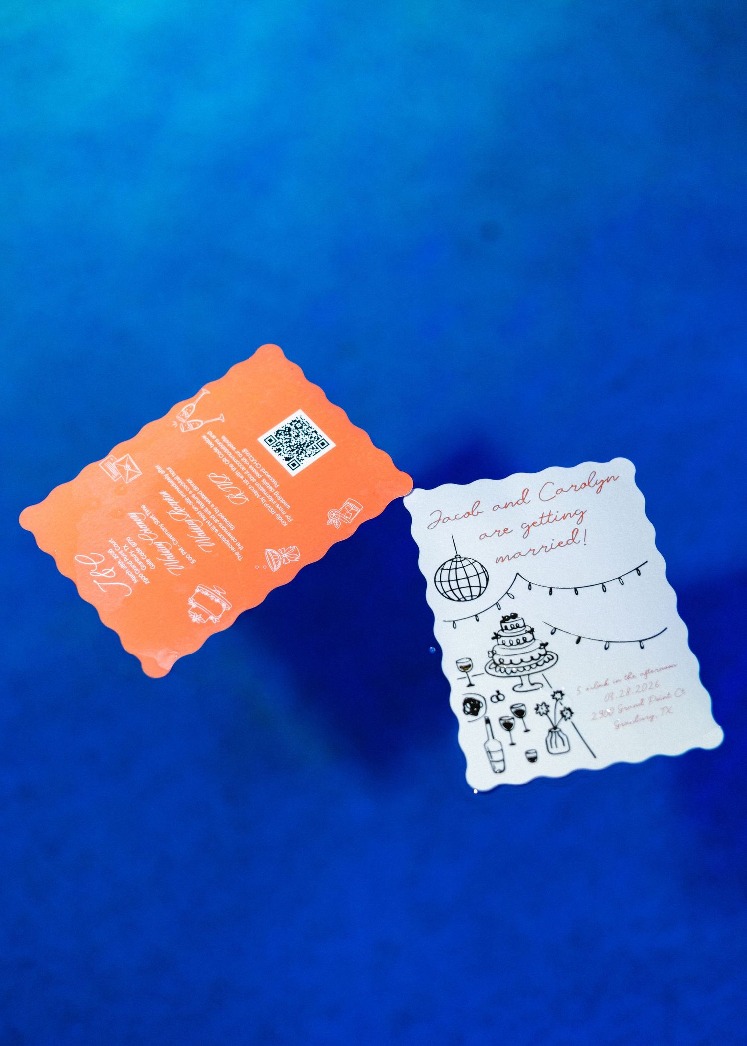 Wedding save-the-date cards with orange scalloped back and white illustrated front on blue background.