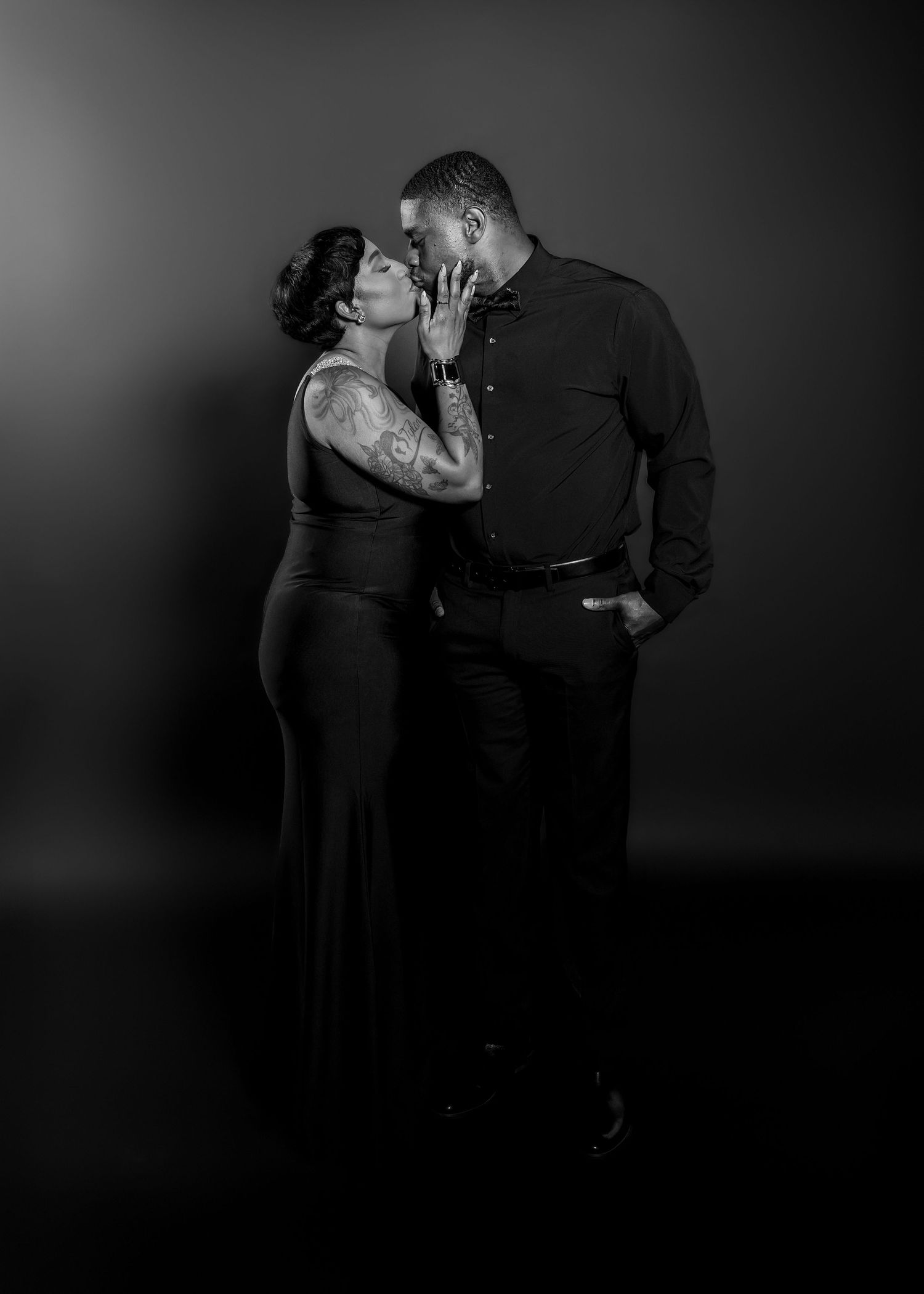 A romantic black and white portrait of a couple sharing an intimate moment in a dark studio setting.