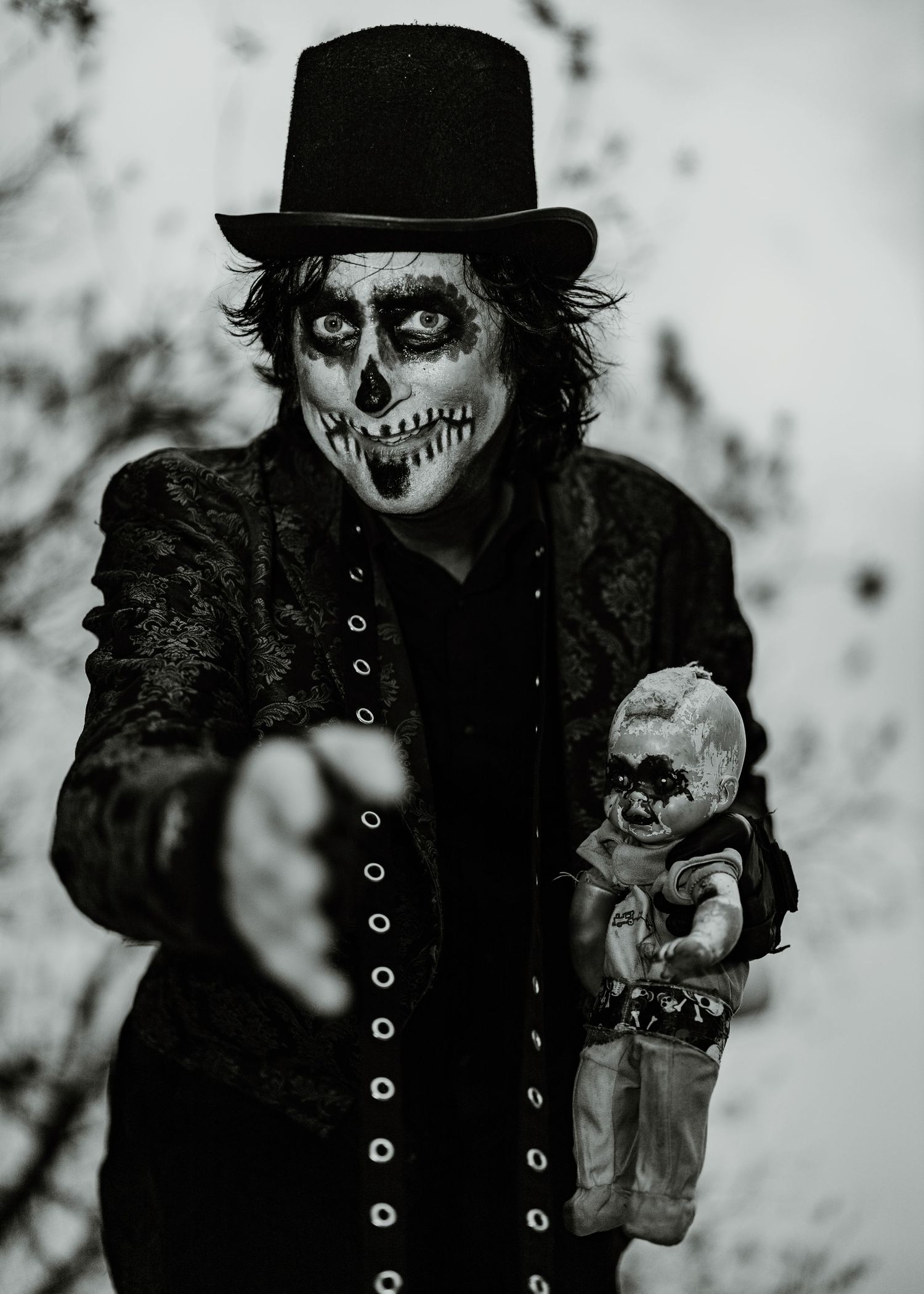 A spooky monochrome portrait of a skeleton-faced figure in a top hat holding a creepy doll.