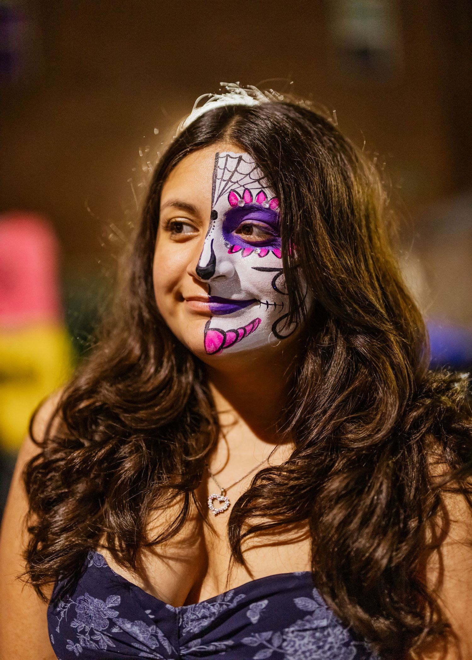 A creative face painting design in purple and white adorns someone wearing dark clothing.