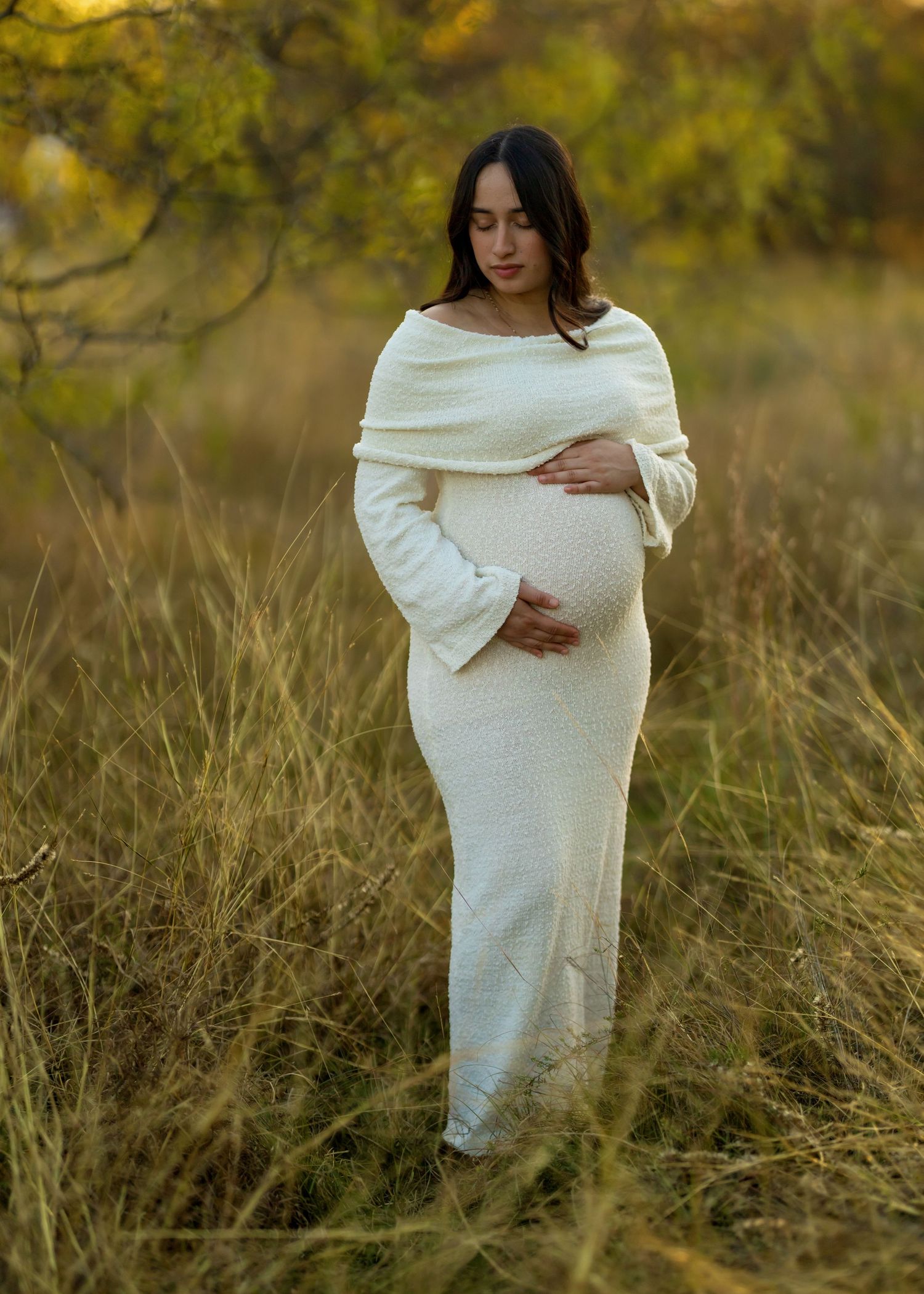Person wearing flowing white fabric poses in a field of tall grass at dusk.
