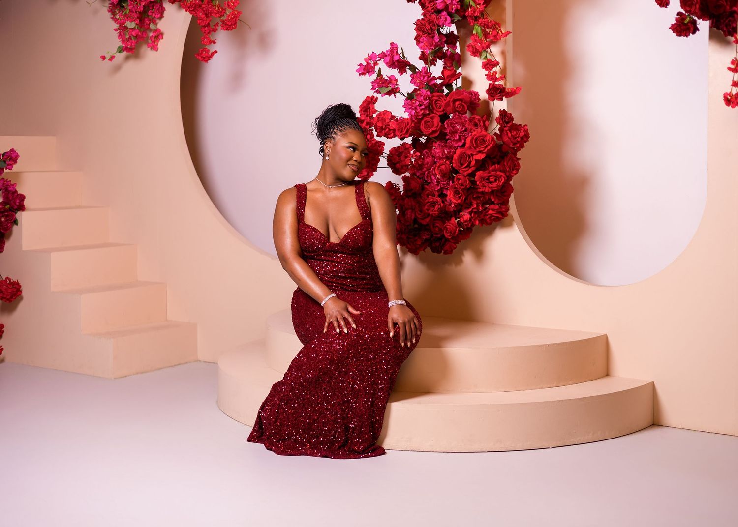A figure in a deep red sequined gown poses elegantly against a beige backdrop with red floral accents.