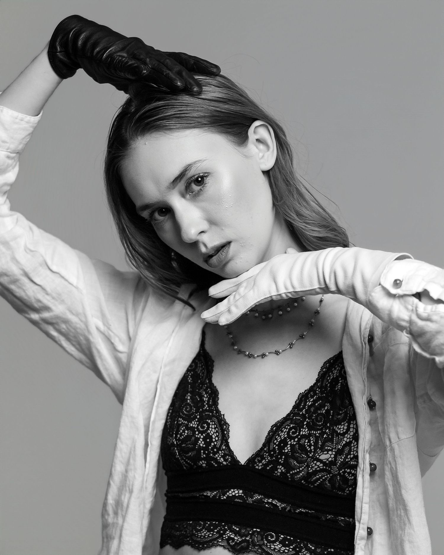 Black and white fashion portrait showing a person in a white button-up shirt and black lace top against a gray background.