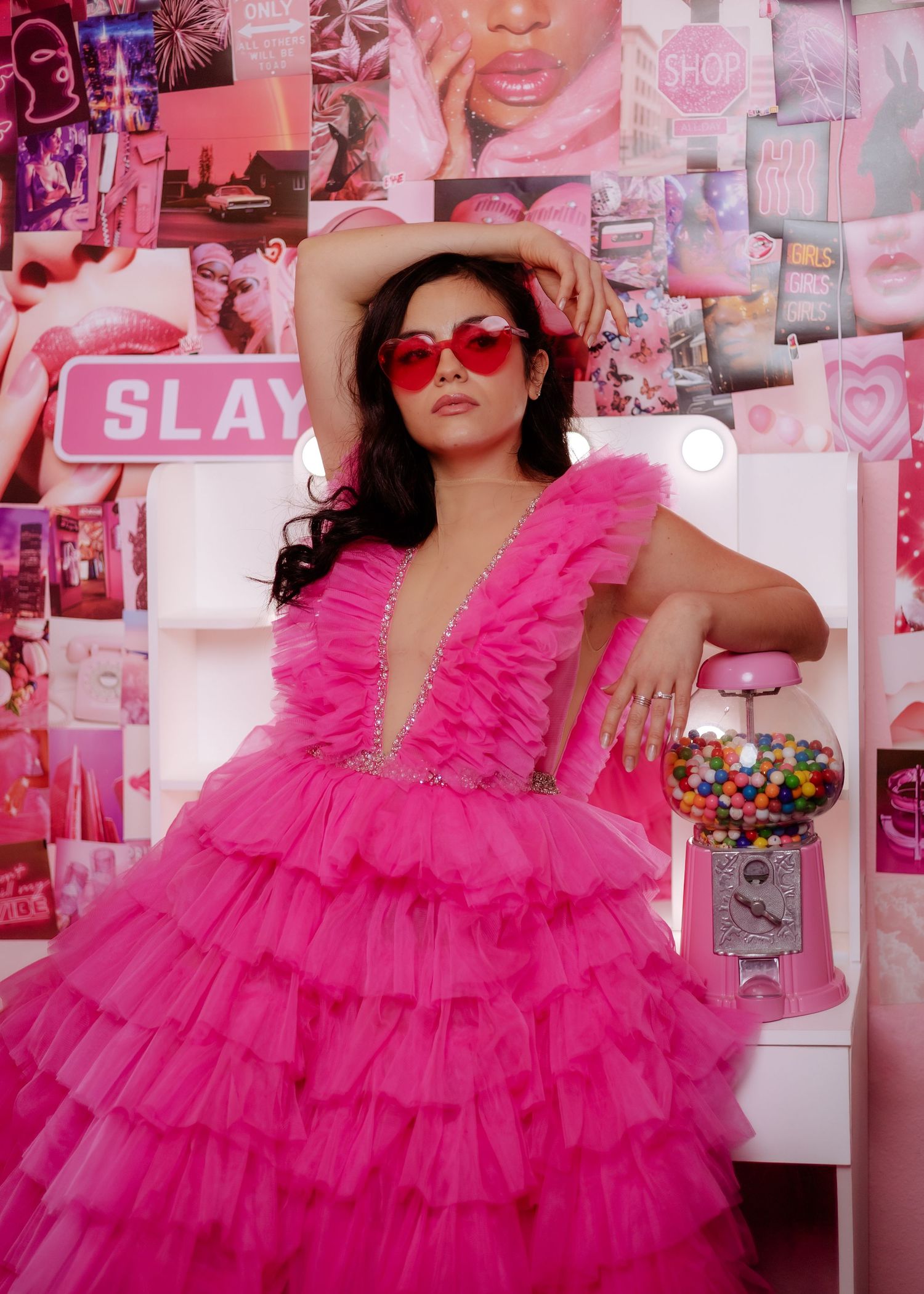 A bright fuchsia ruffled dress is showcased in a pink-themed room with decorative wall collages.