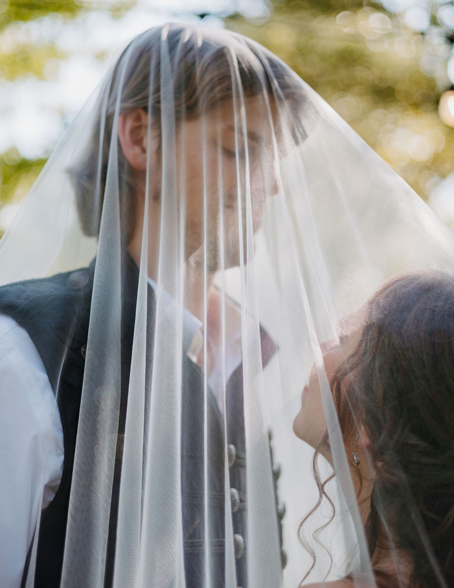 Bride and groom share an intimate moment under a flowing white wedding veil during their outdoor ceremony.
