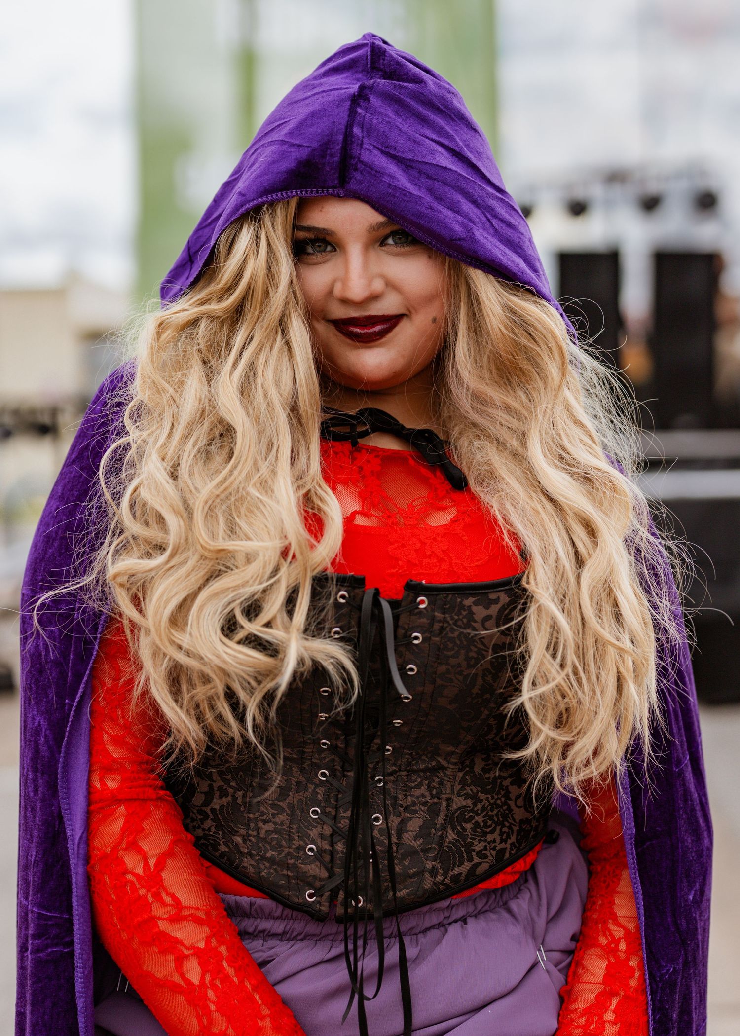Fashion portrait with purple hood, blonde hair, and red lace details in moody lighting.