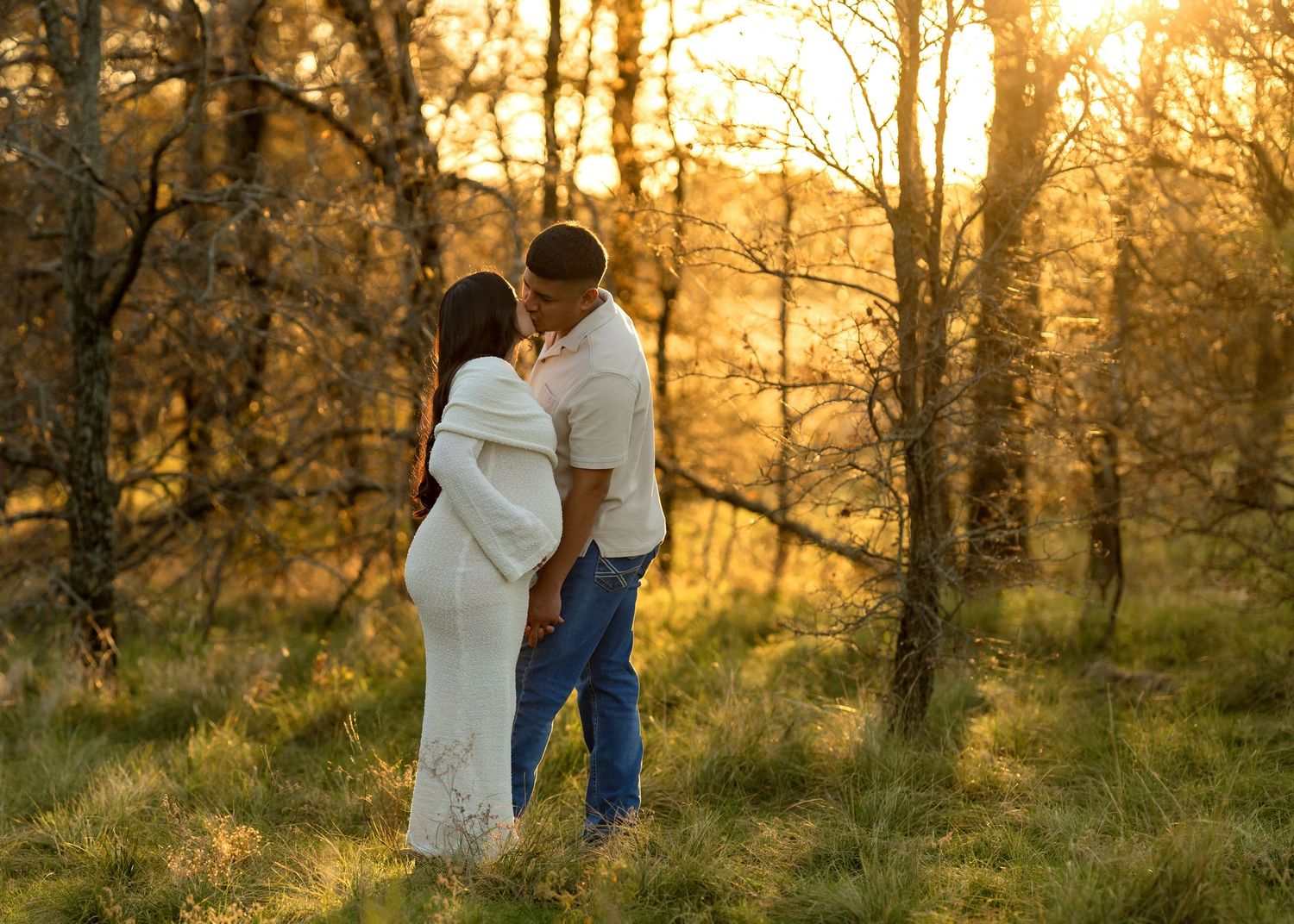 Couple embraces in a golden forest during sunset with sunlight streaming through autumn trees.