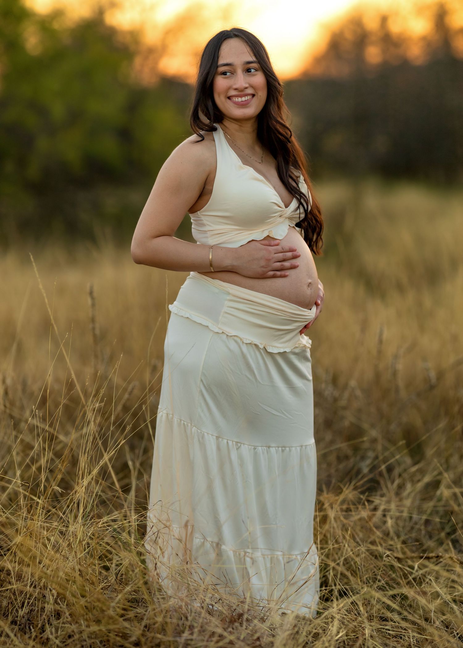 Maternity photo in a white dress against natural golden hour lighting.