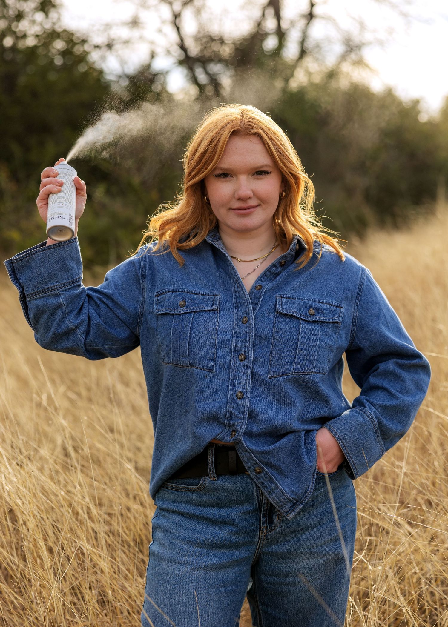 Person in denim jacket posing in field of tall grass at sunset.