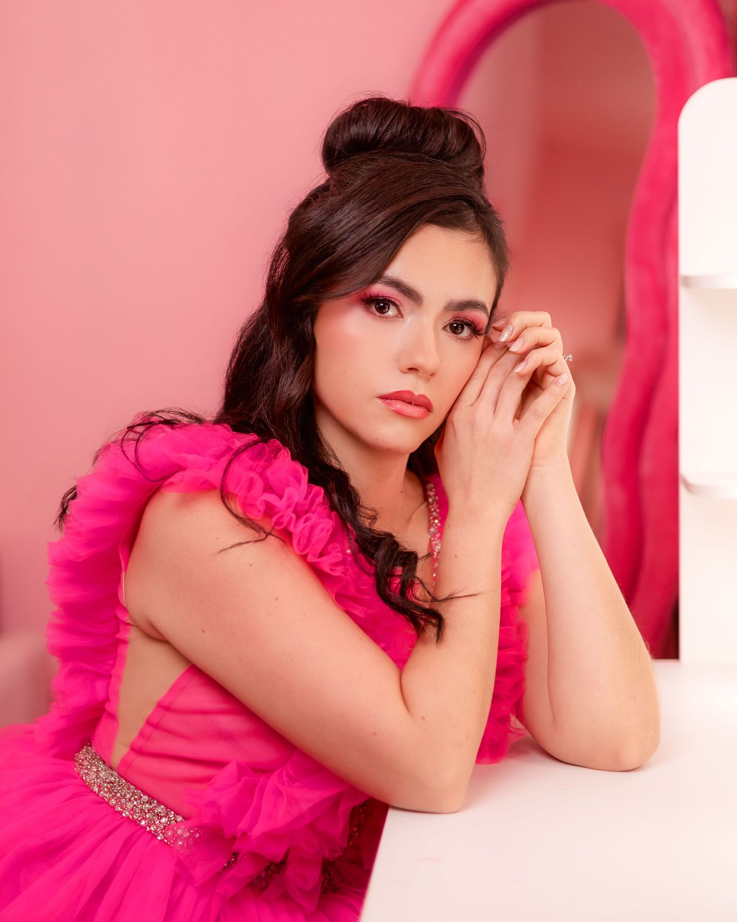 A woman in a vibrant hot pink dress poses gracefully against a pink backdrop in a glamorous photo session.