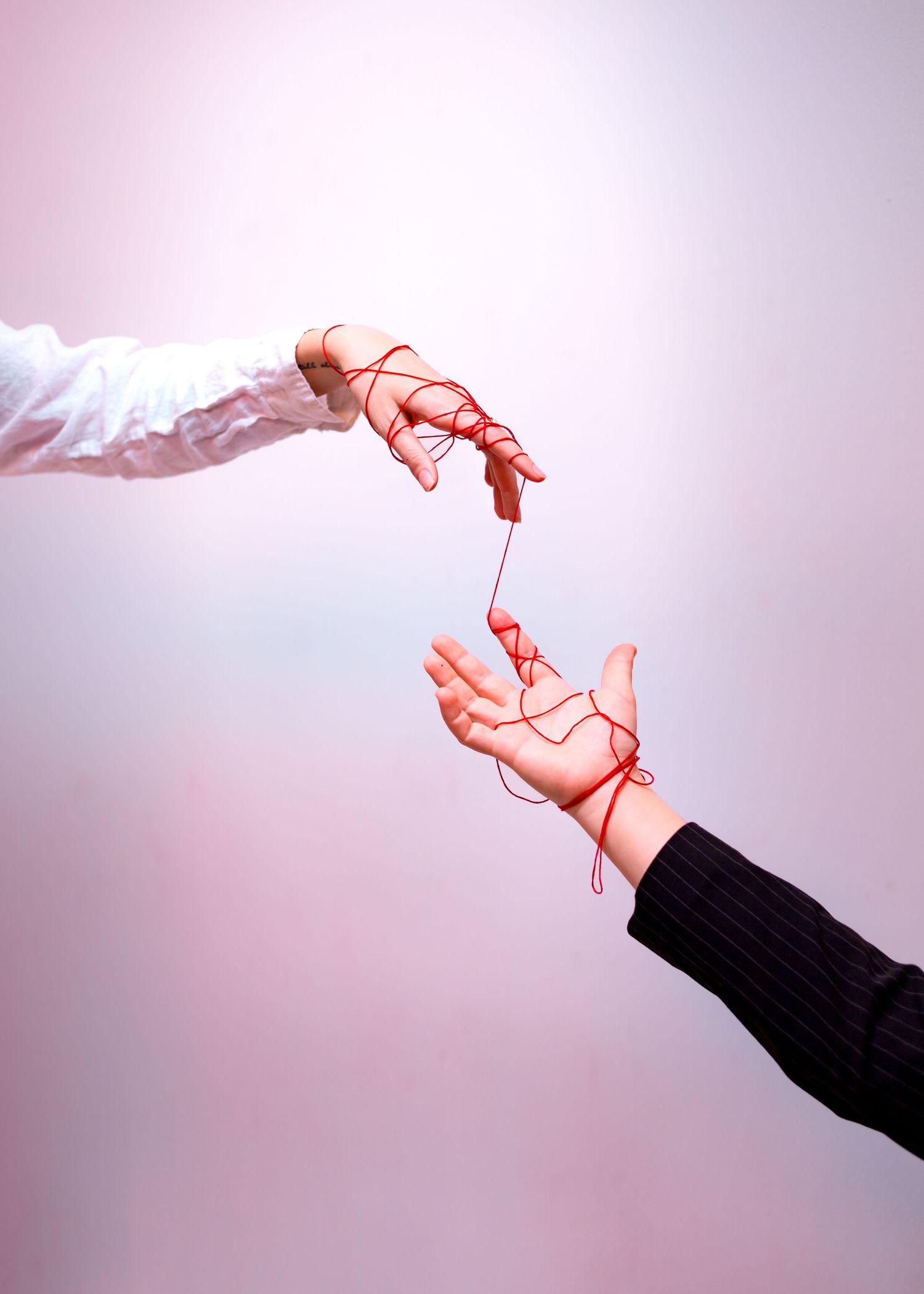 Abstract hand gestures against pink background showing graceful movement and red string.